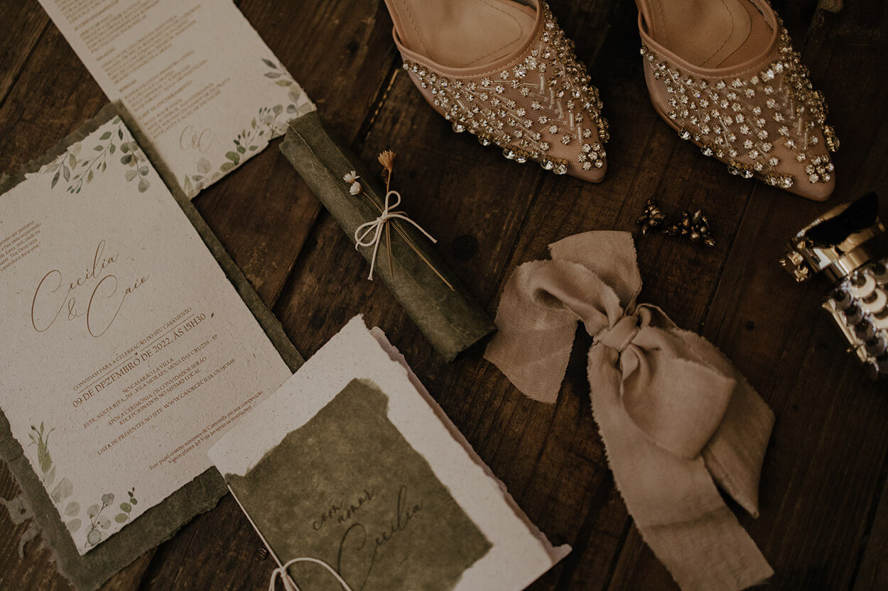 Convite de casamento e sapato bege com joias sobre a mesa