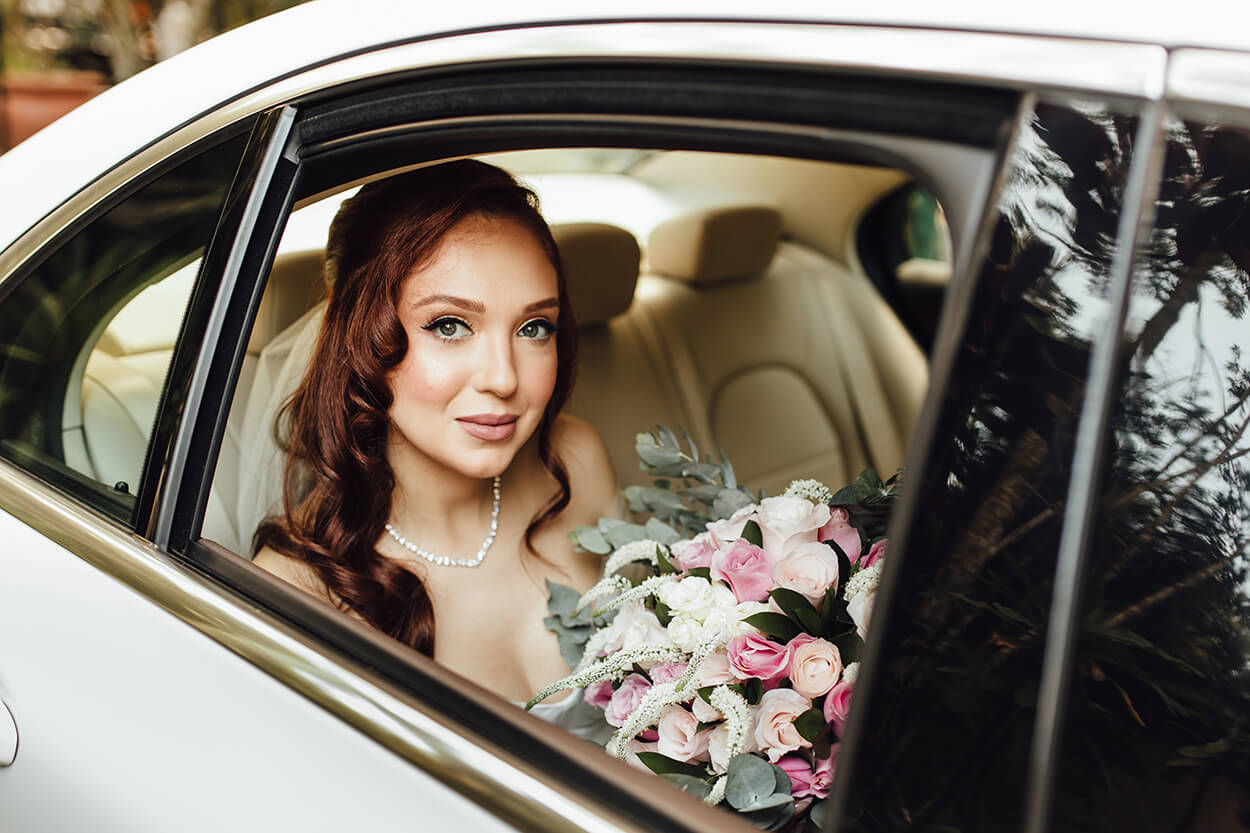 Noiva ddentro do carro segurando buquê com flores rosas e brancas