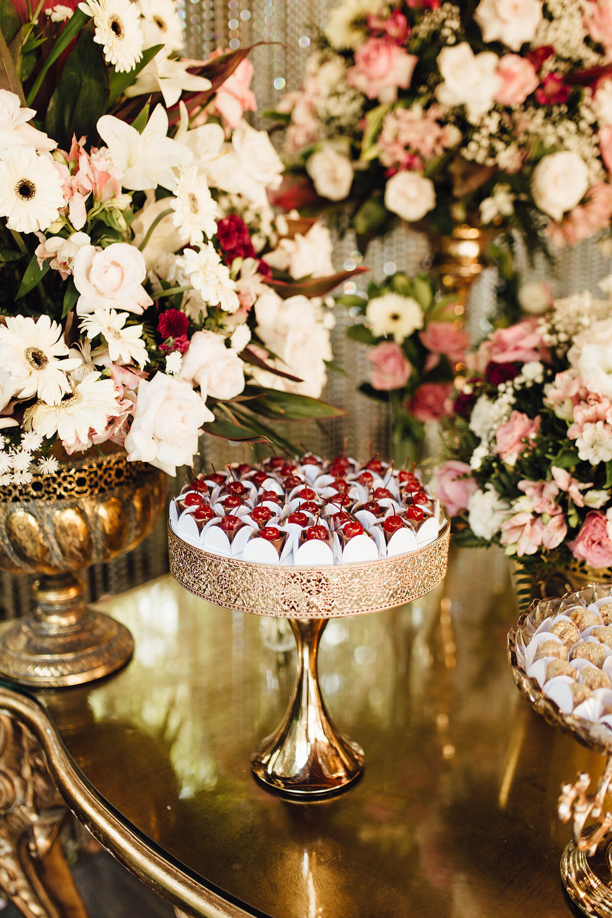 Mesa dourada com bandejas com doces de casamento e flores brnacas e rosas