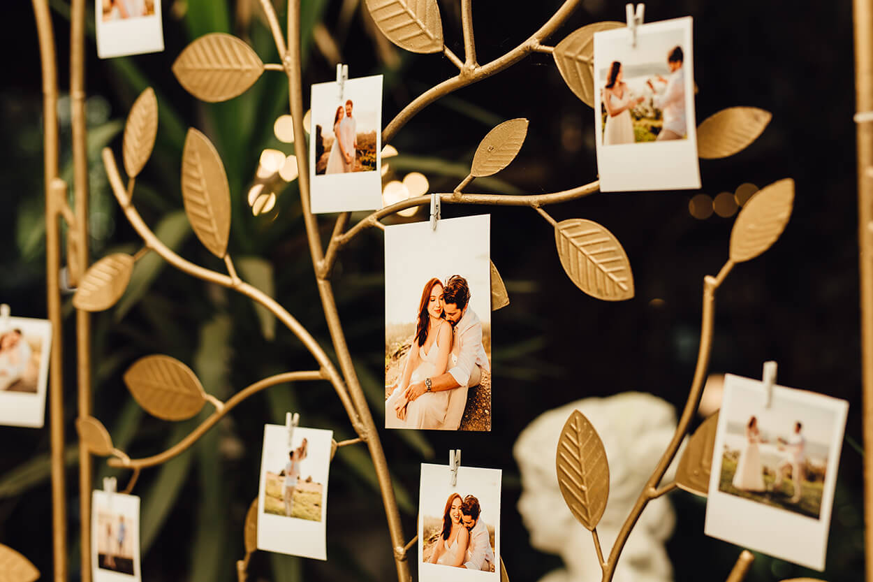 Painel dourado com galhos e folhas e fotos instantâneas do casal