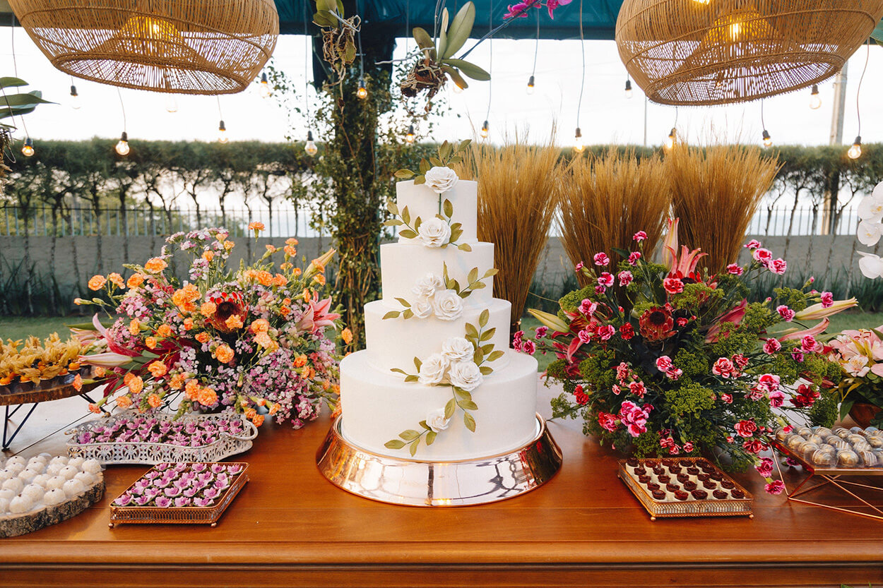 Mesa de madeira com bolo de casamento com quatro andares decorado com flores brancas