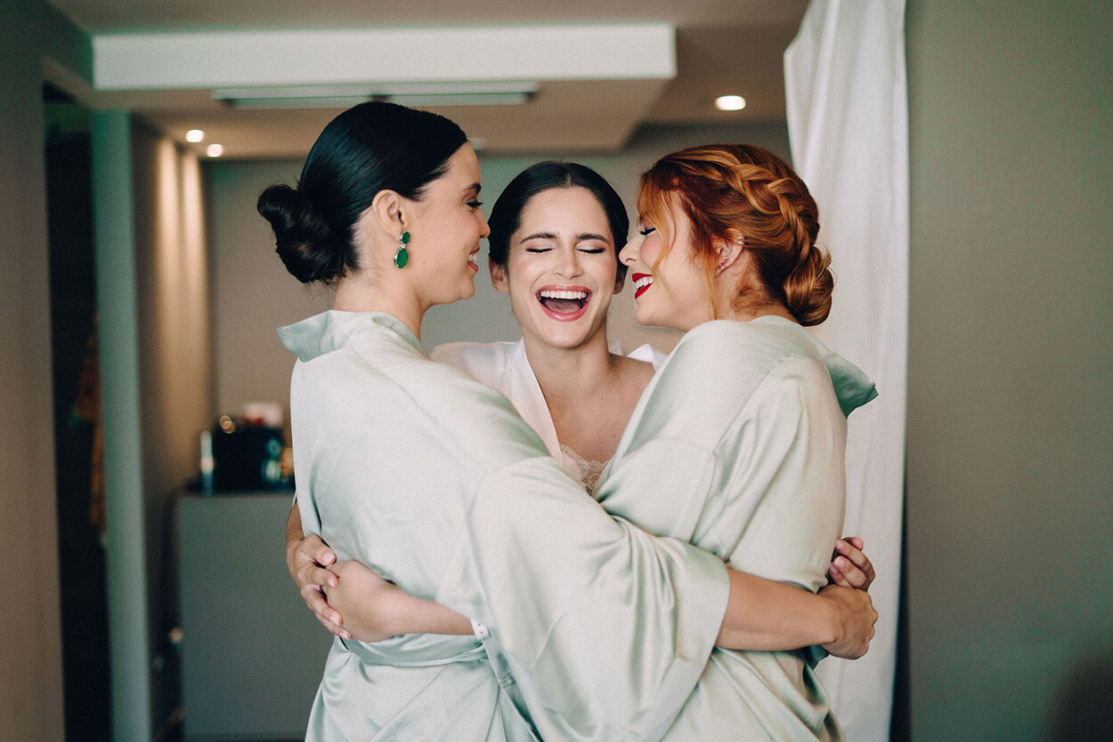 Noiva abraçando duas mulheres vestindo robes