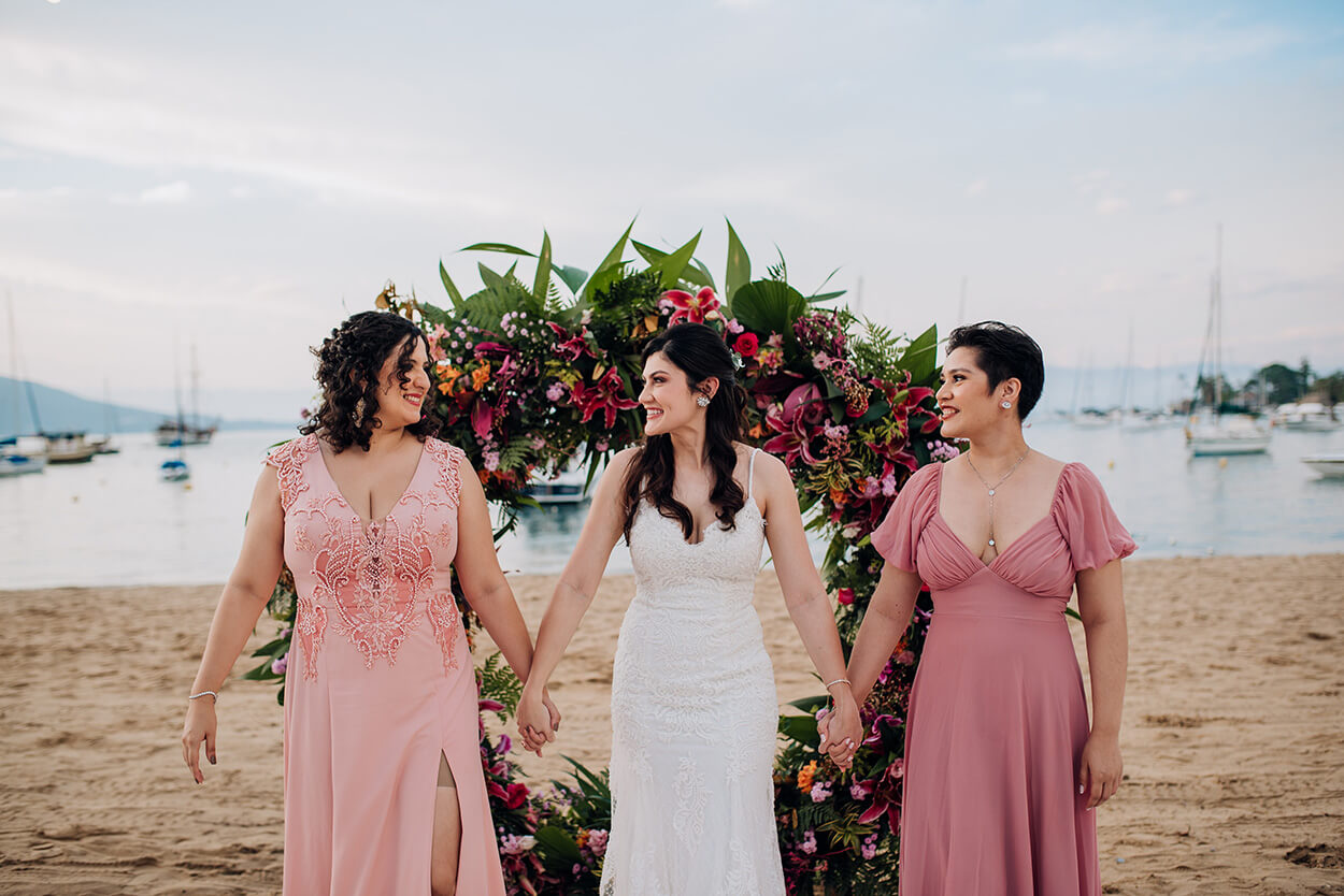 Noiva de mãos dadas com duas mulheres com vestidos rose