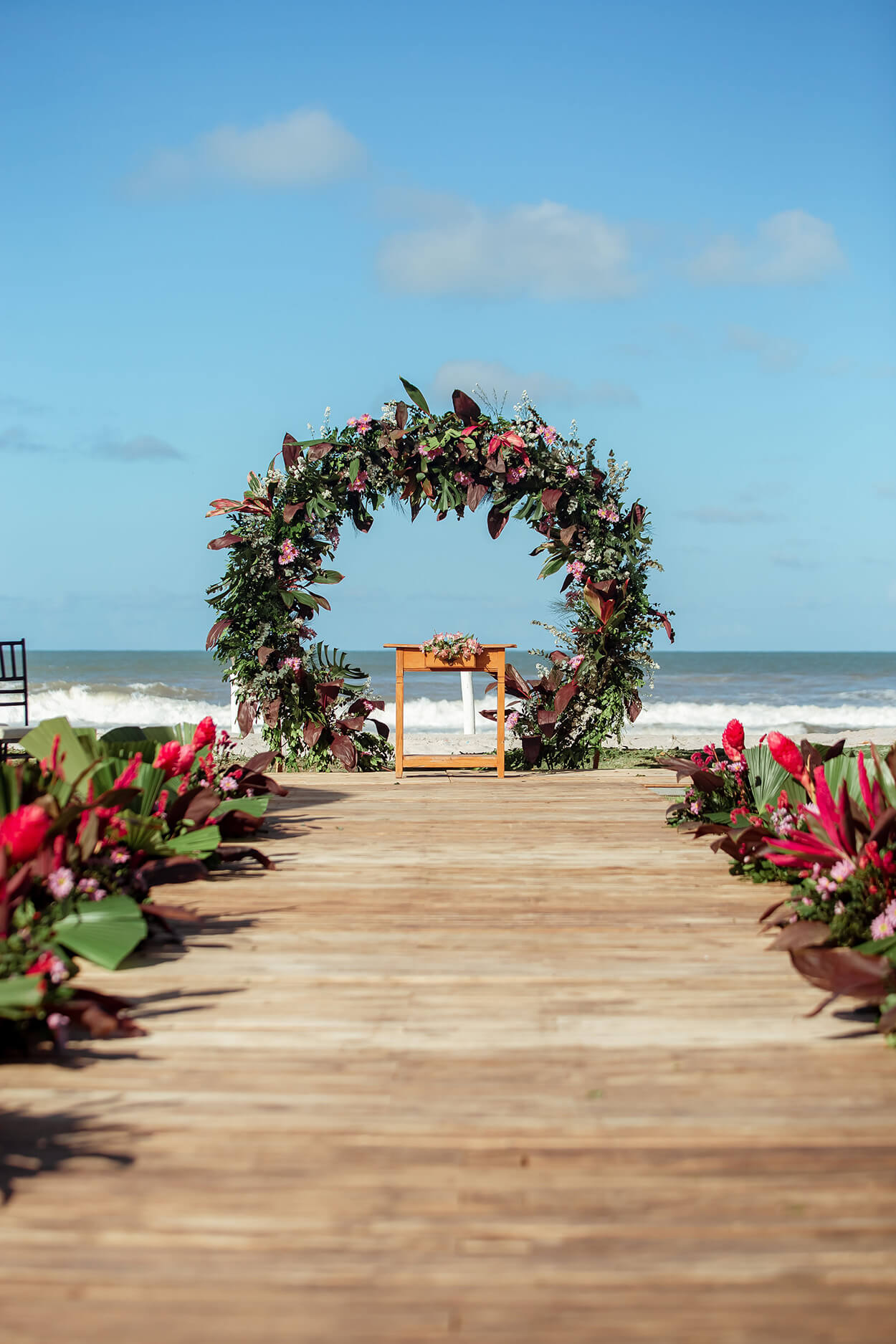Altar redondo com flores rosas e folhagens verde de frente para a praia