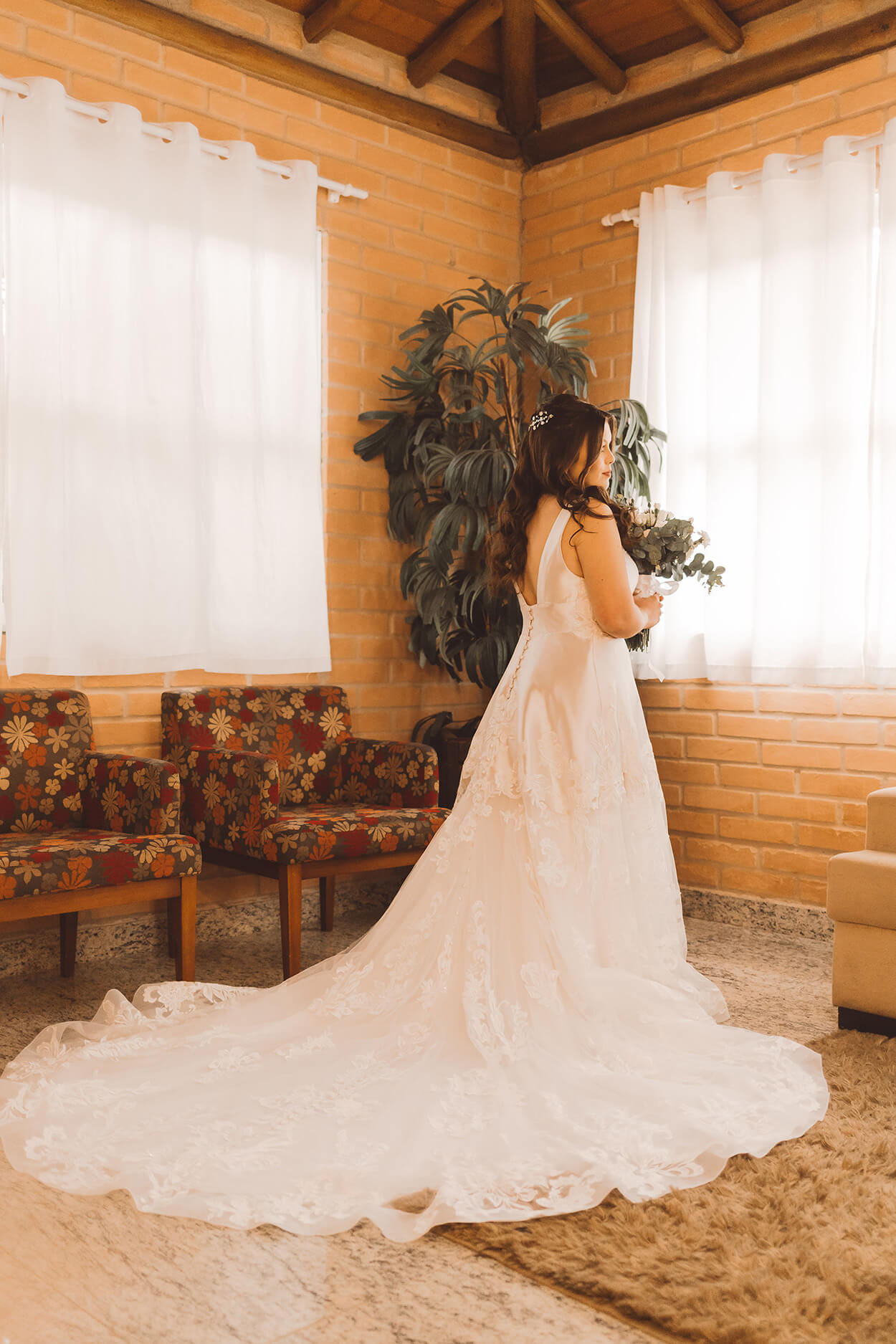 Mulher com vestido de noiva com cauda longa dentro da sala rústica