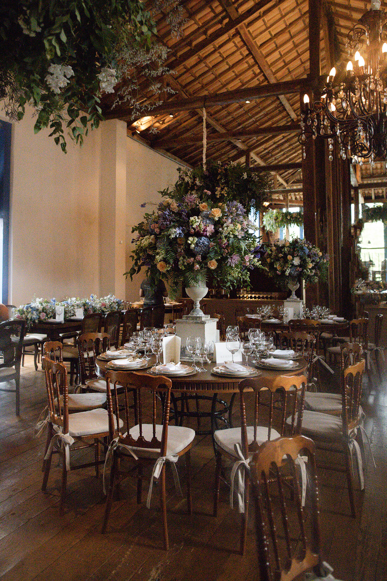 Salao rustico com mesas de madeira redonda com vasos com flores coloridas