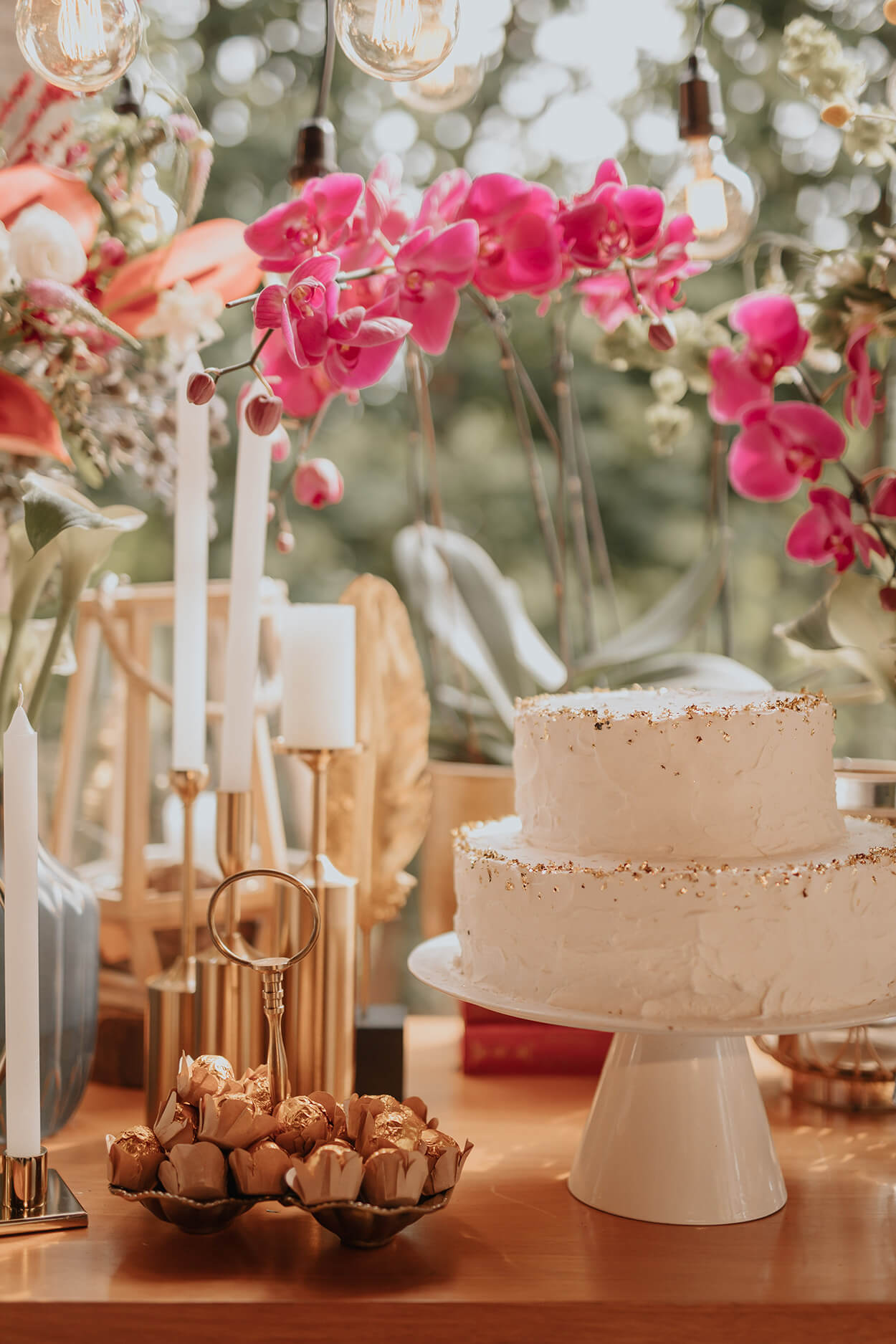 bolo de casamento redondo branco de dois andares ao lado de castiçais dourados com velas