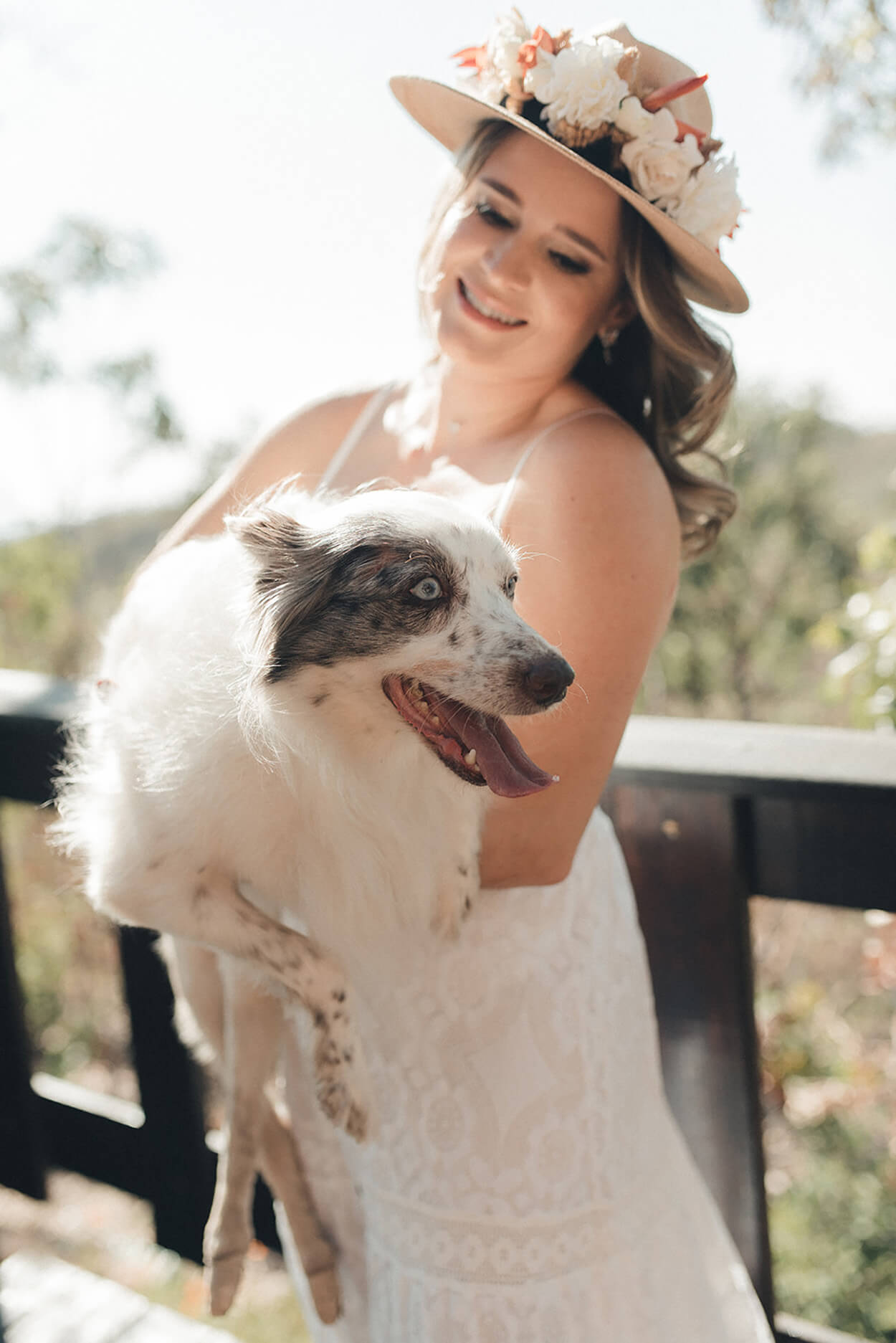 Noiva com chapeu marrom com flores segurando cachorro branco no colo