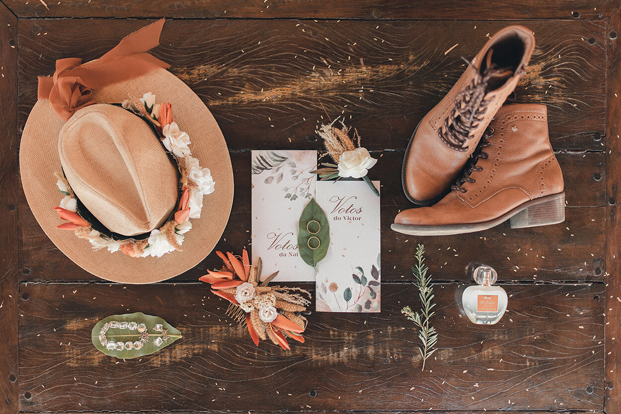 Mesa de madeira com chapeu marrom com flores e convite de casamento branco e botas marrom