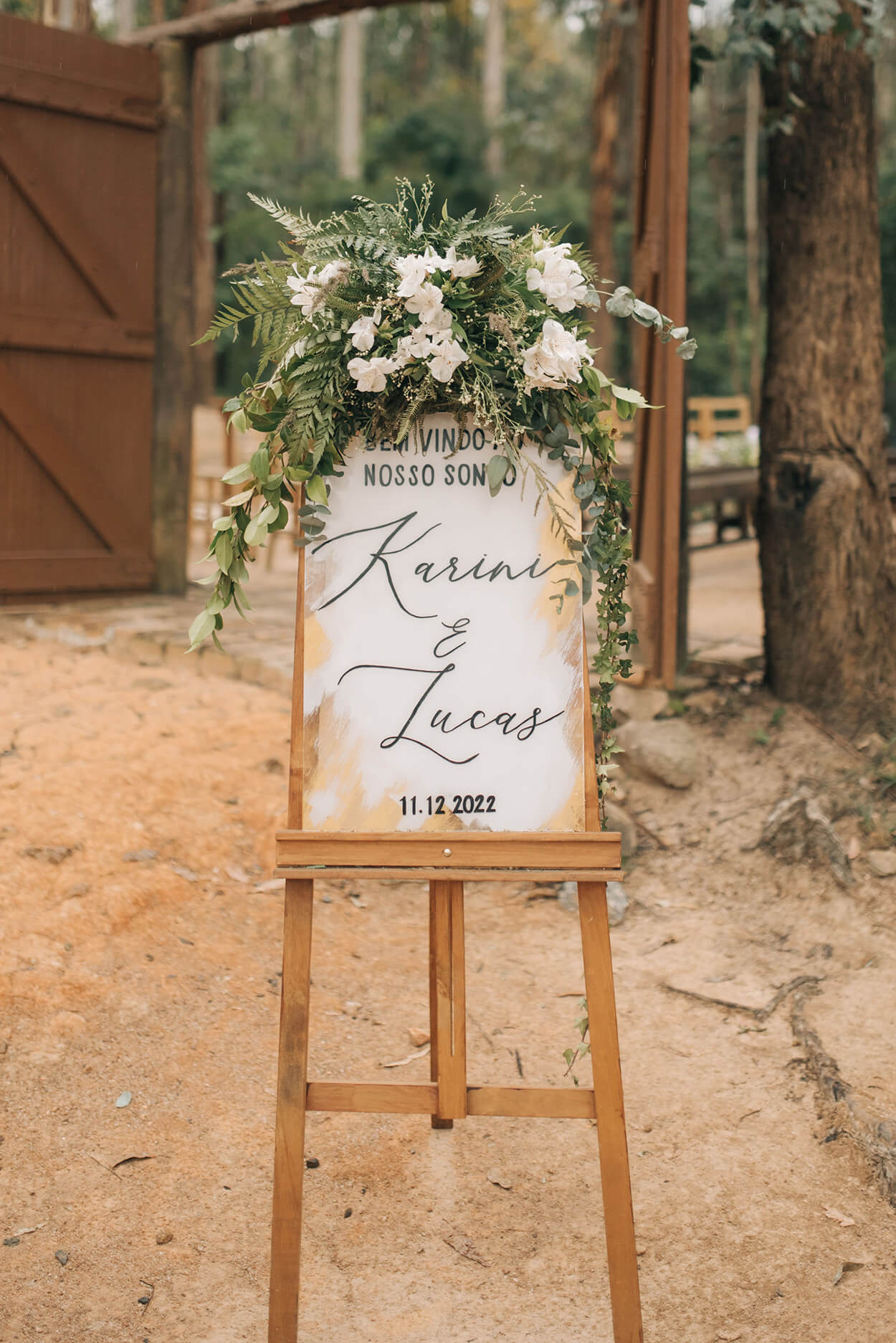 Cavalete de madeira com quadro branco escrito nome dos noivos e arranjo floral branco