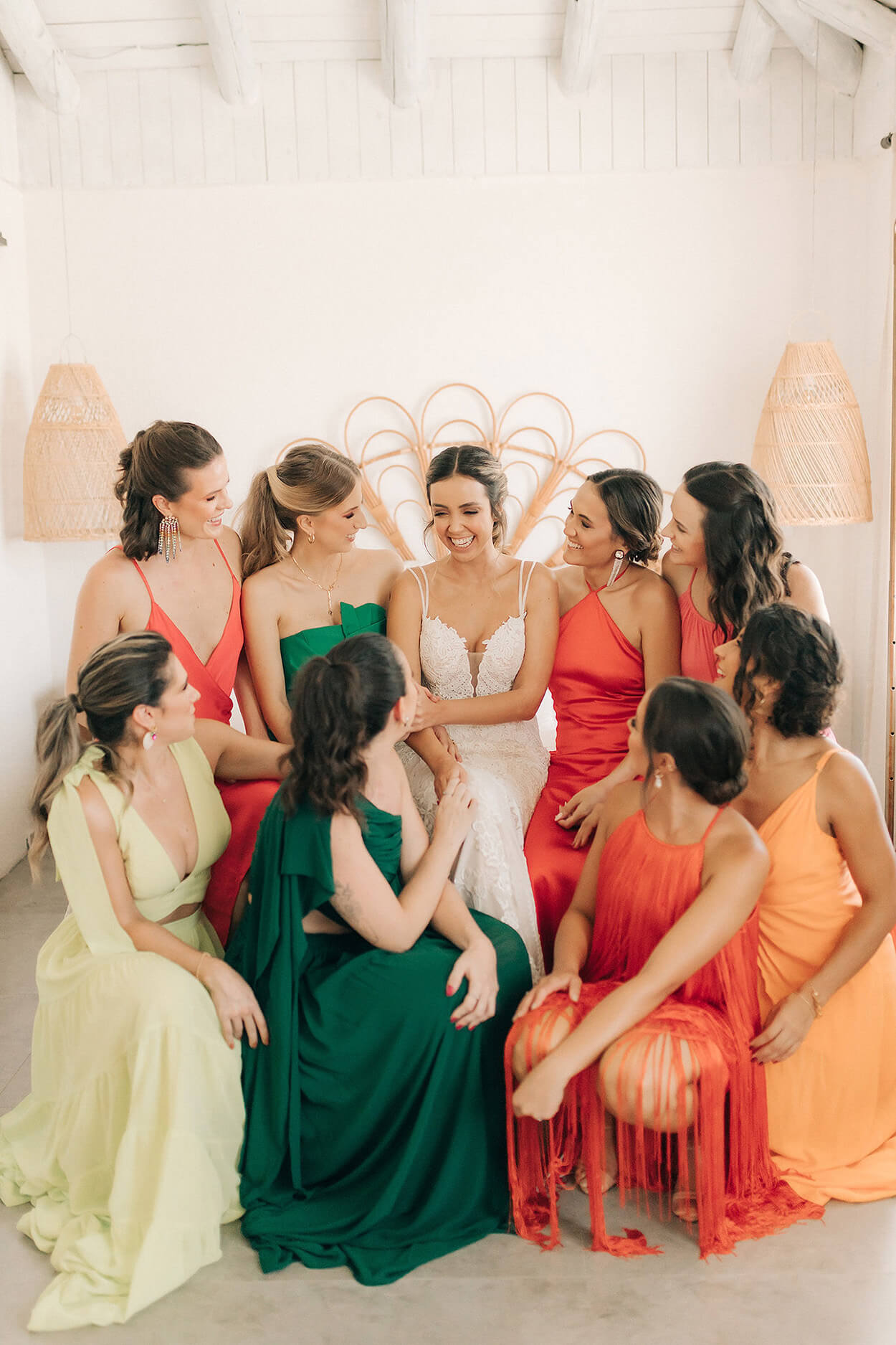 Madrinhas com vestido verdes laranjas e amarelo ao redor da noiva