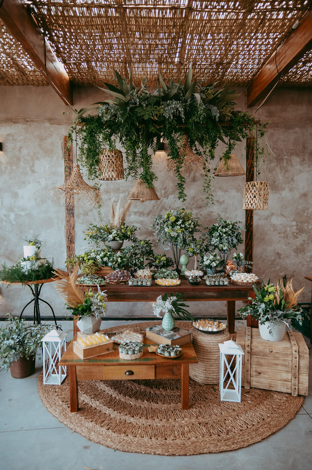 Salão com mesa com vasos de flores e folhagens e doces de casamento