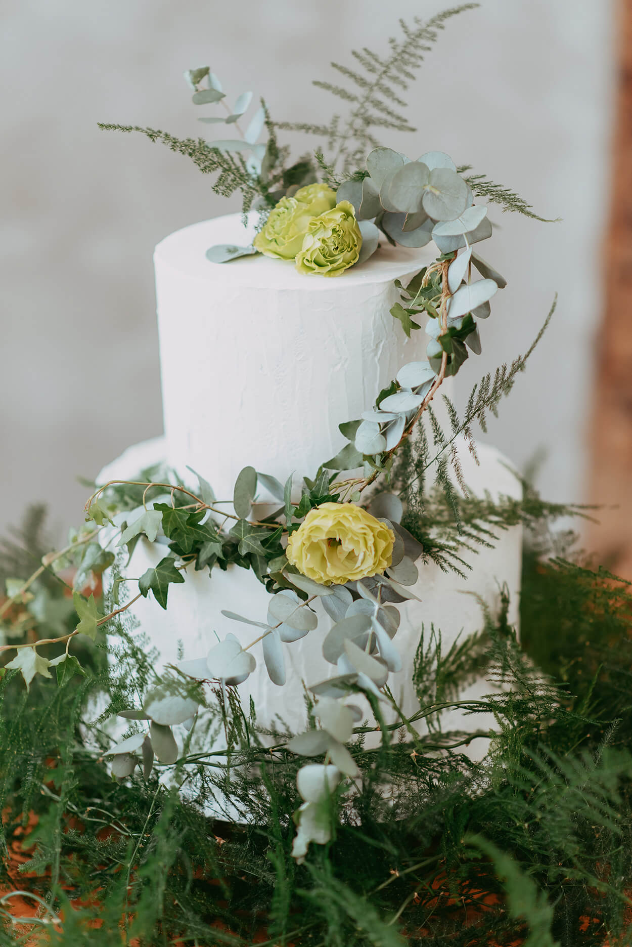 Bolo de casamento branco com dois andraes e topo com flor verde ramos de eucalipto e de pinheiro