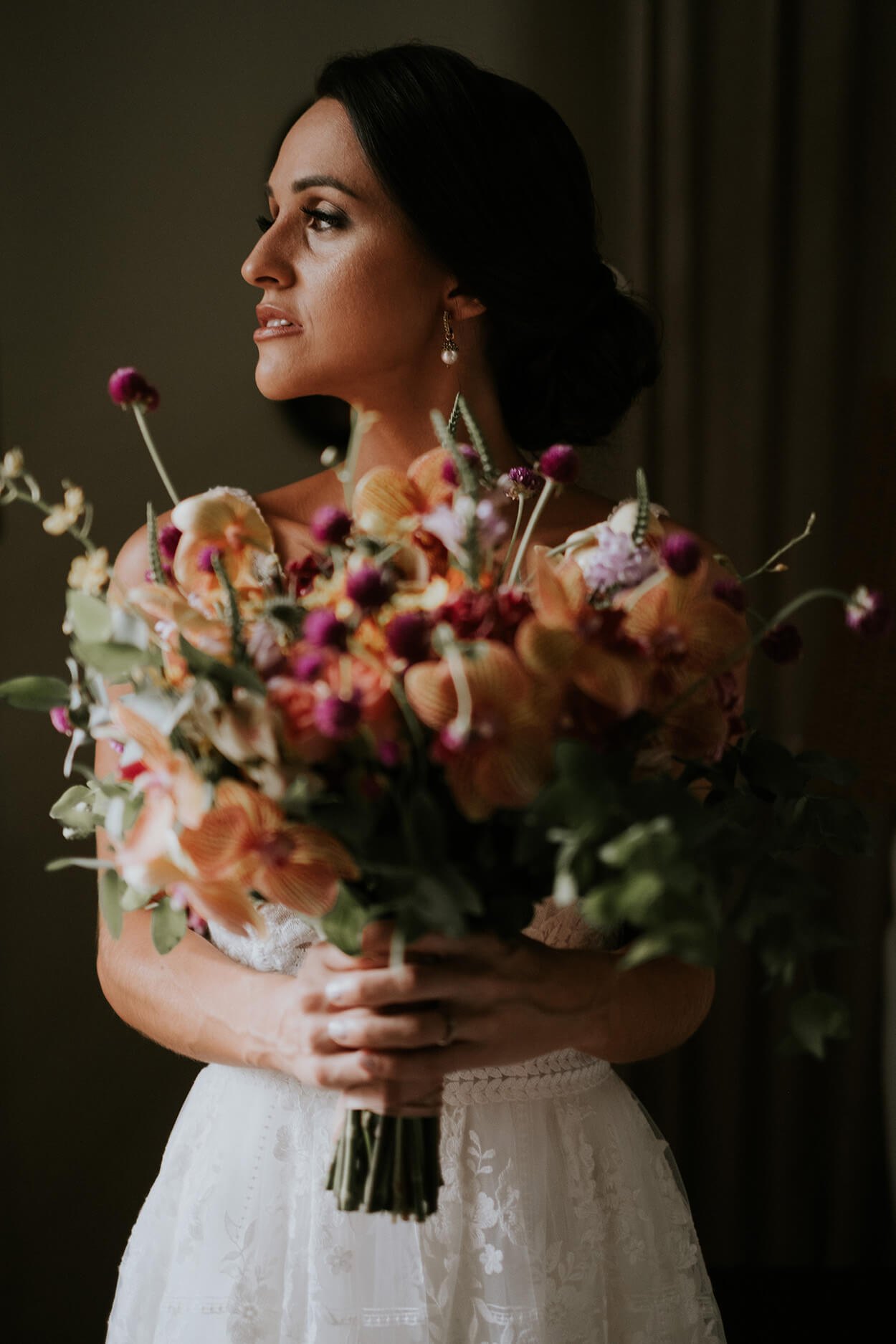 noiva com cabelo preso segurando buquê com flores laranjas e roxas