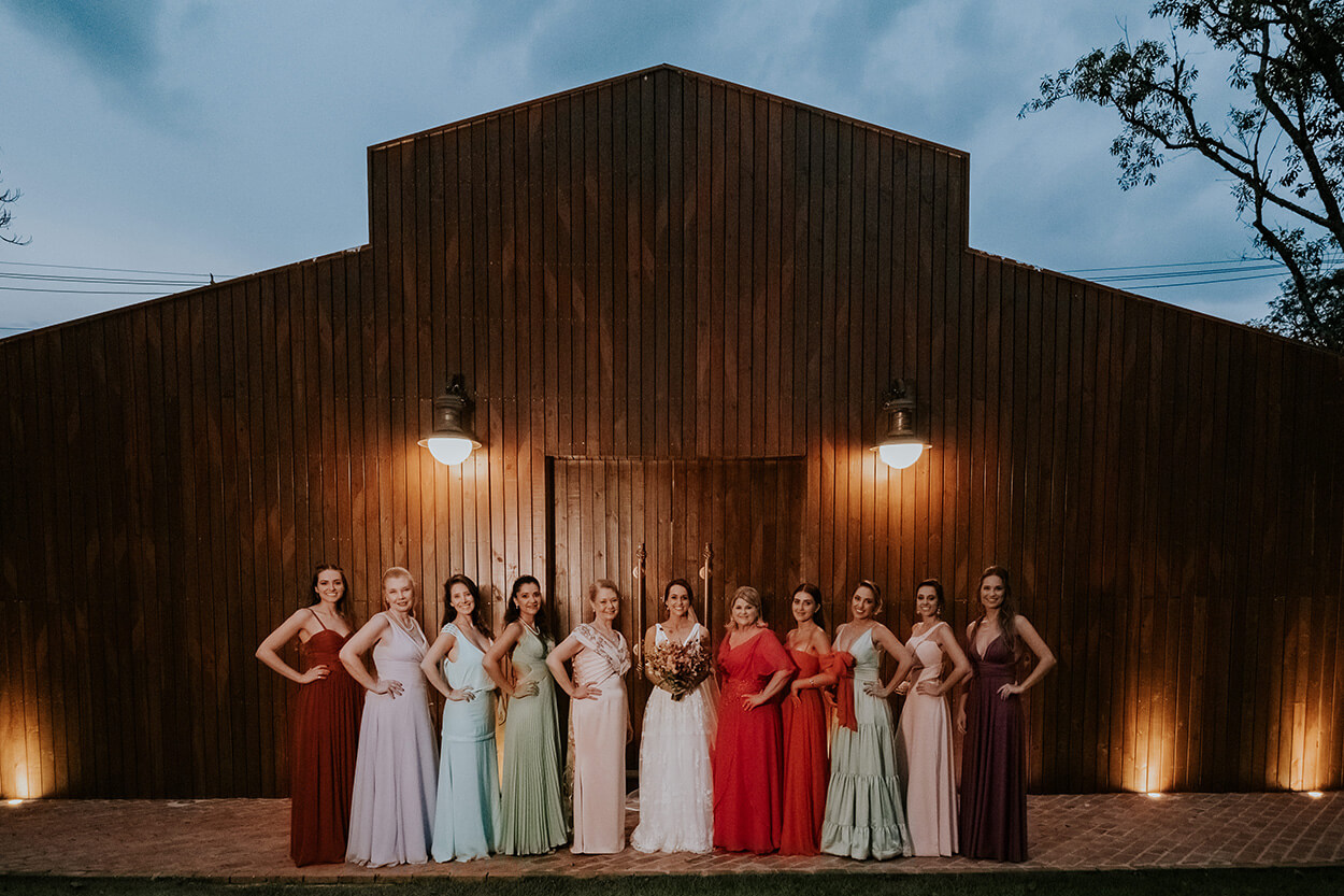 Noiva e madrinhas com vestidos coloridos na frente de galpão rústico