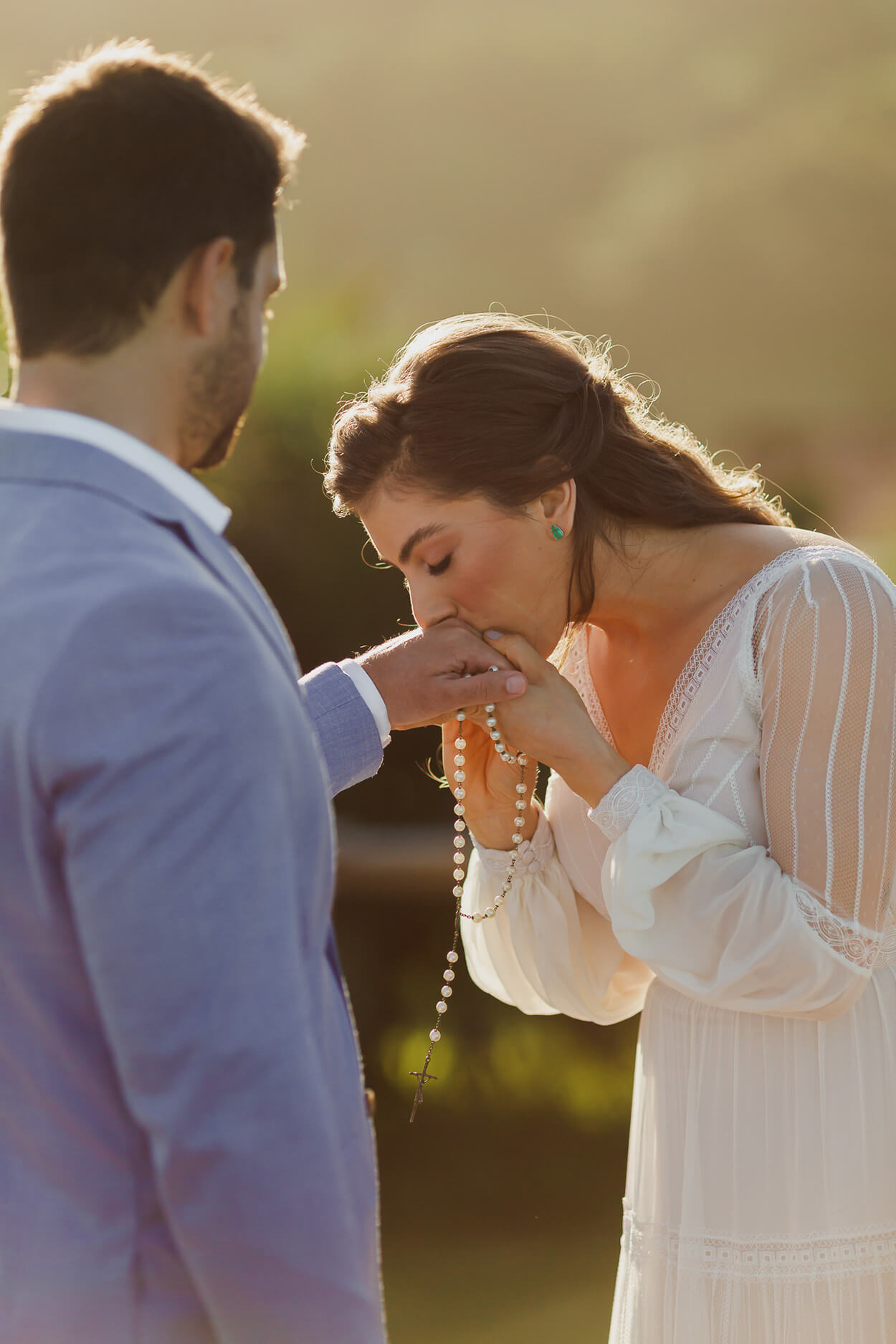 Noiva segurando um terço e beijando a mão do noivo