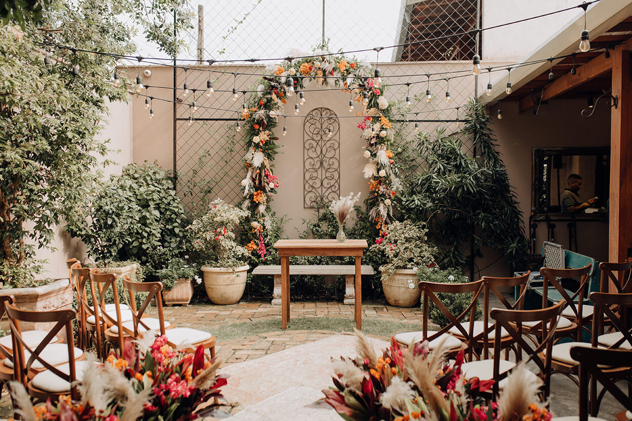 cadeiras e flores de frente para altar com arco de flores coloridas no jardim