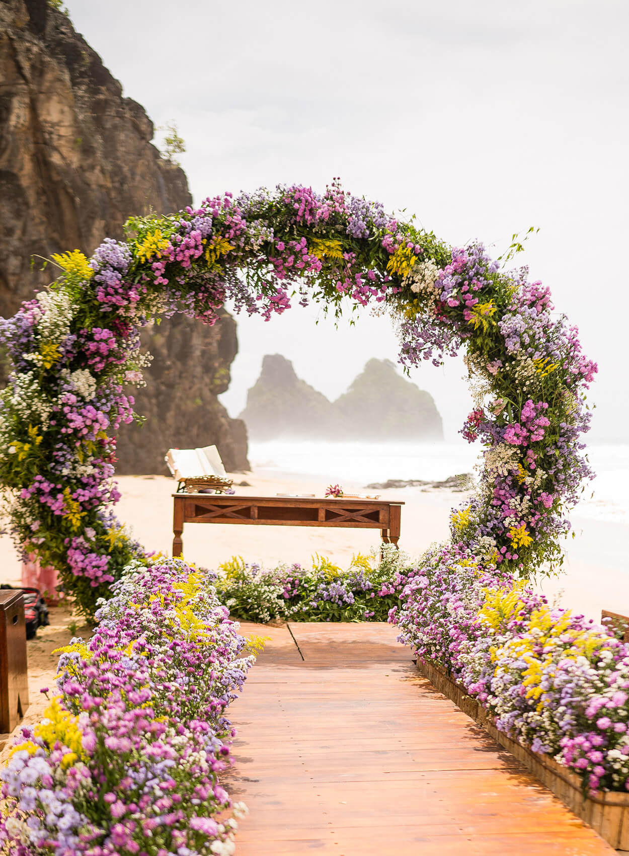 altar na praia com arco com flores brancas lilas lavanda e amarelas