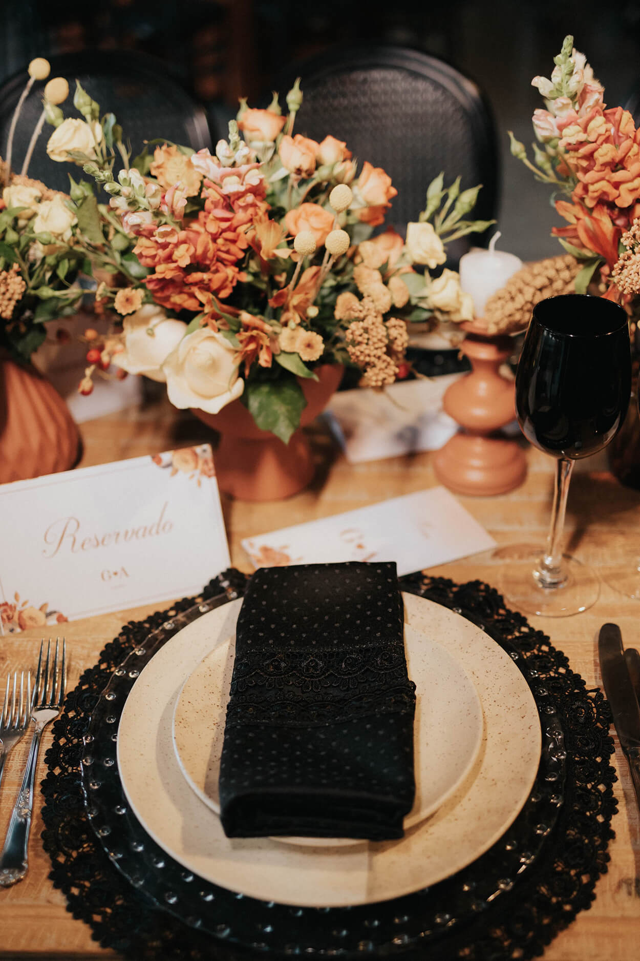mesa posta com sousplat e guardanapo preto e flores laranjas