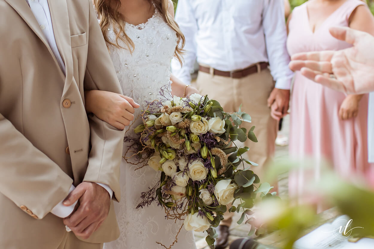 noivos de baços dados e noiva segurando buque com flores brancas e roxas