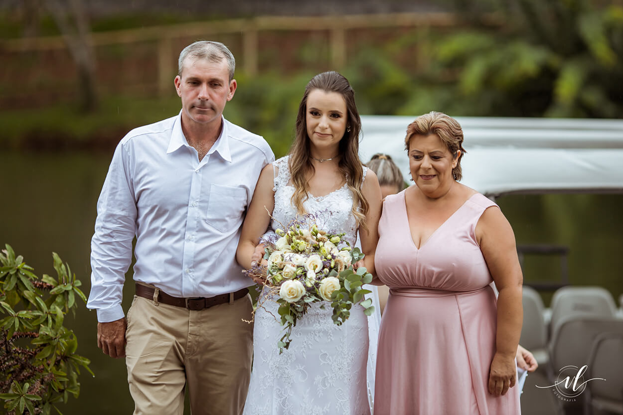 entrada da noiva ao lado de seu pai com calça bege e camisa branca e mãe com vetsido rosa claro