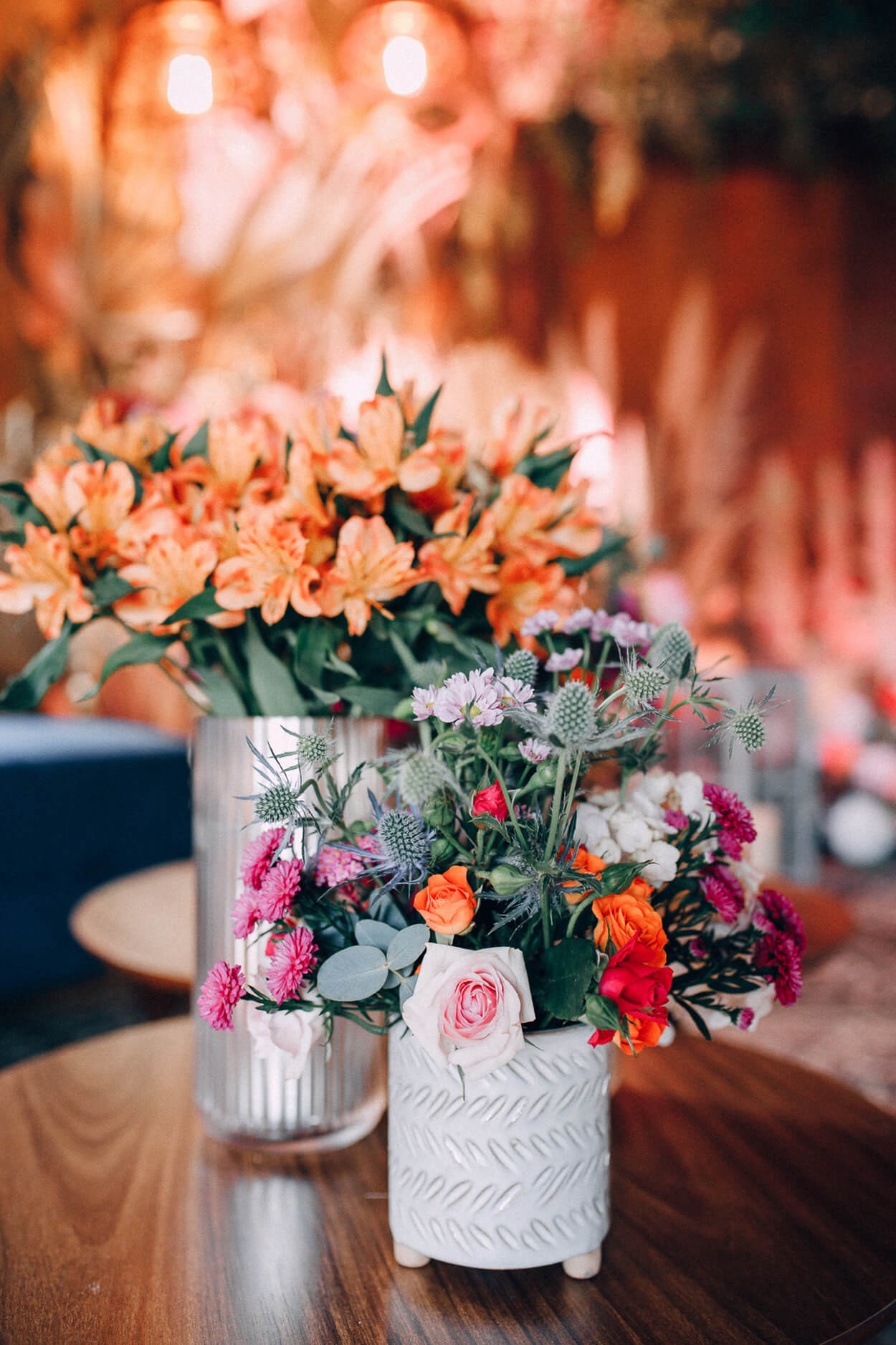 mesa de madeira com dois vasos com flores laranjas e rosas