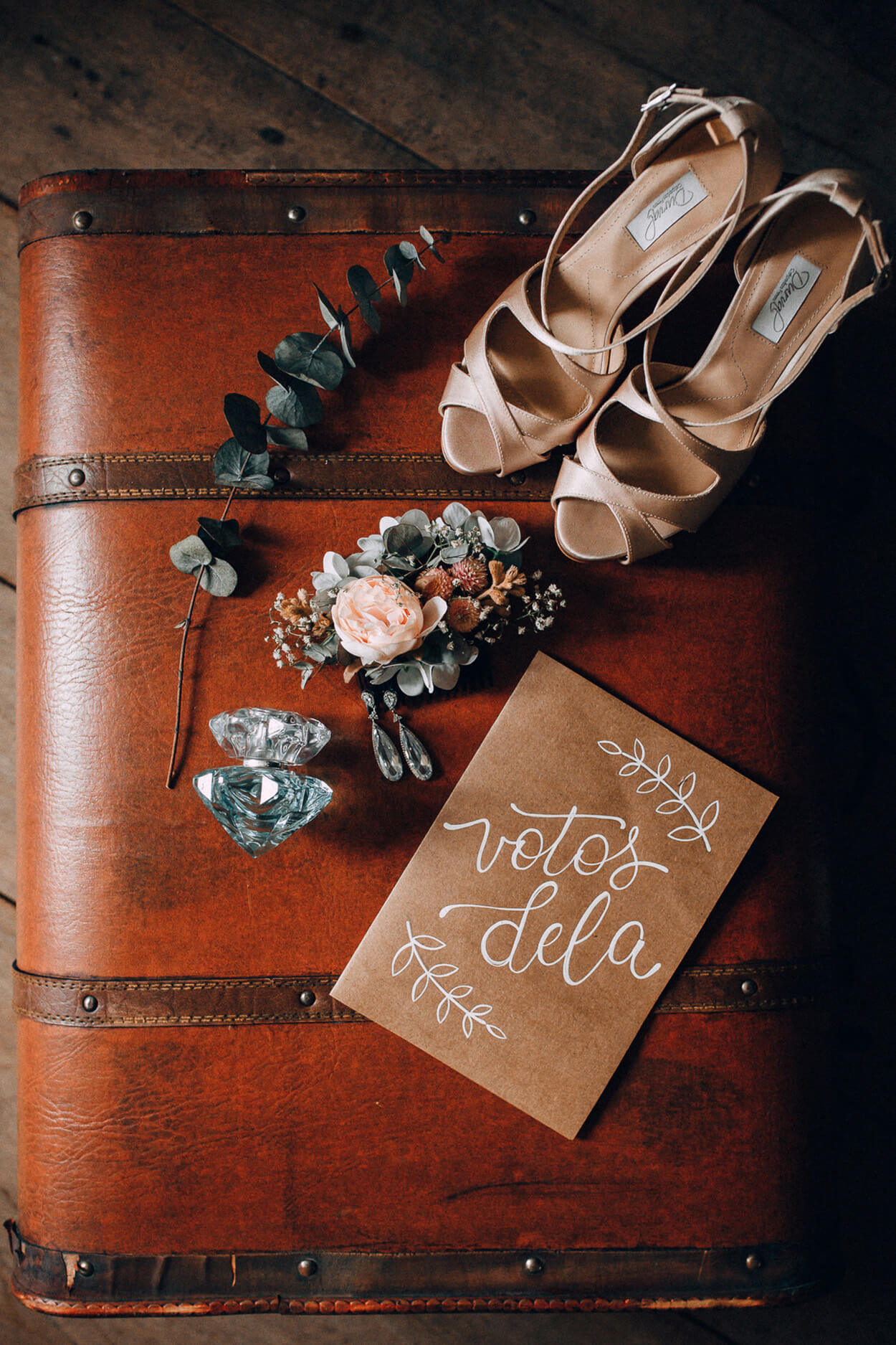 Sandália branca e ramos de flores em cima da mala de couro e caderno de votos em papel pardo