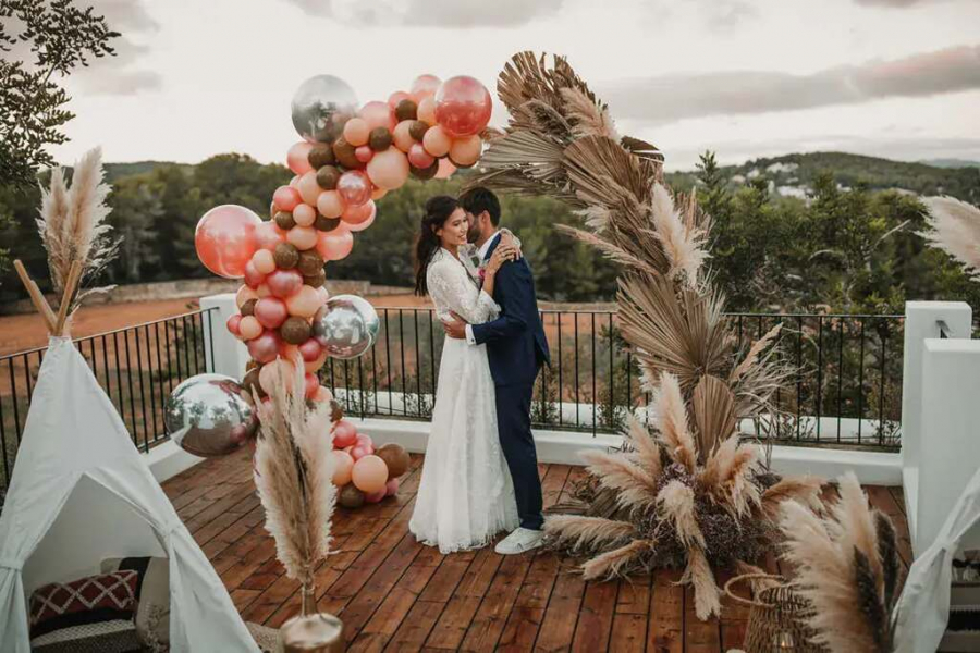 noivos abraçados com altar de balões e folhagens secas