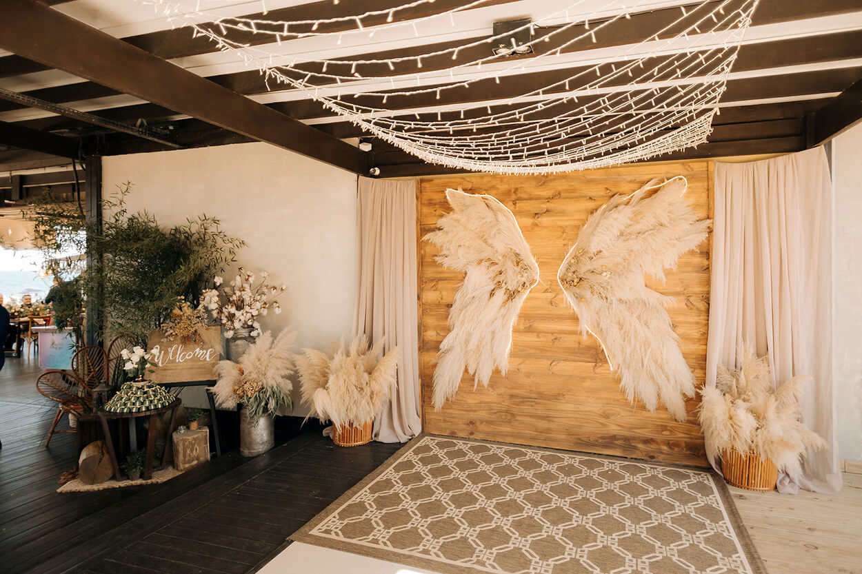 salão com parede instagramavel com painel de madeira e asas feitas com capim dos pampas