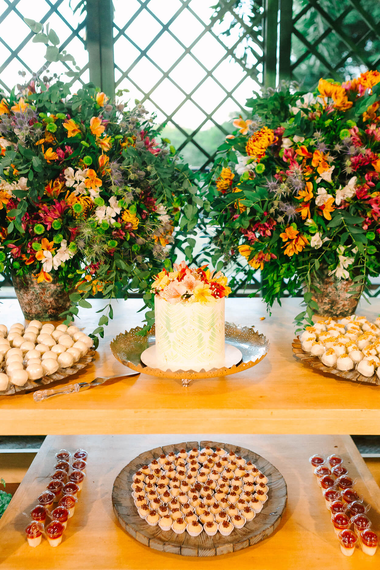 Mesa de madeira com bolo de casamento branco com flores coloridas e bandeja com doces