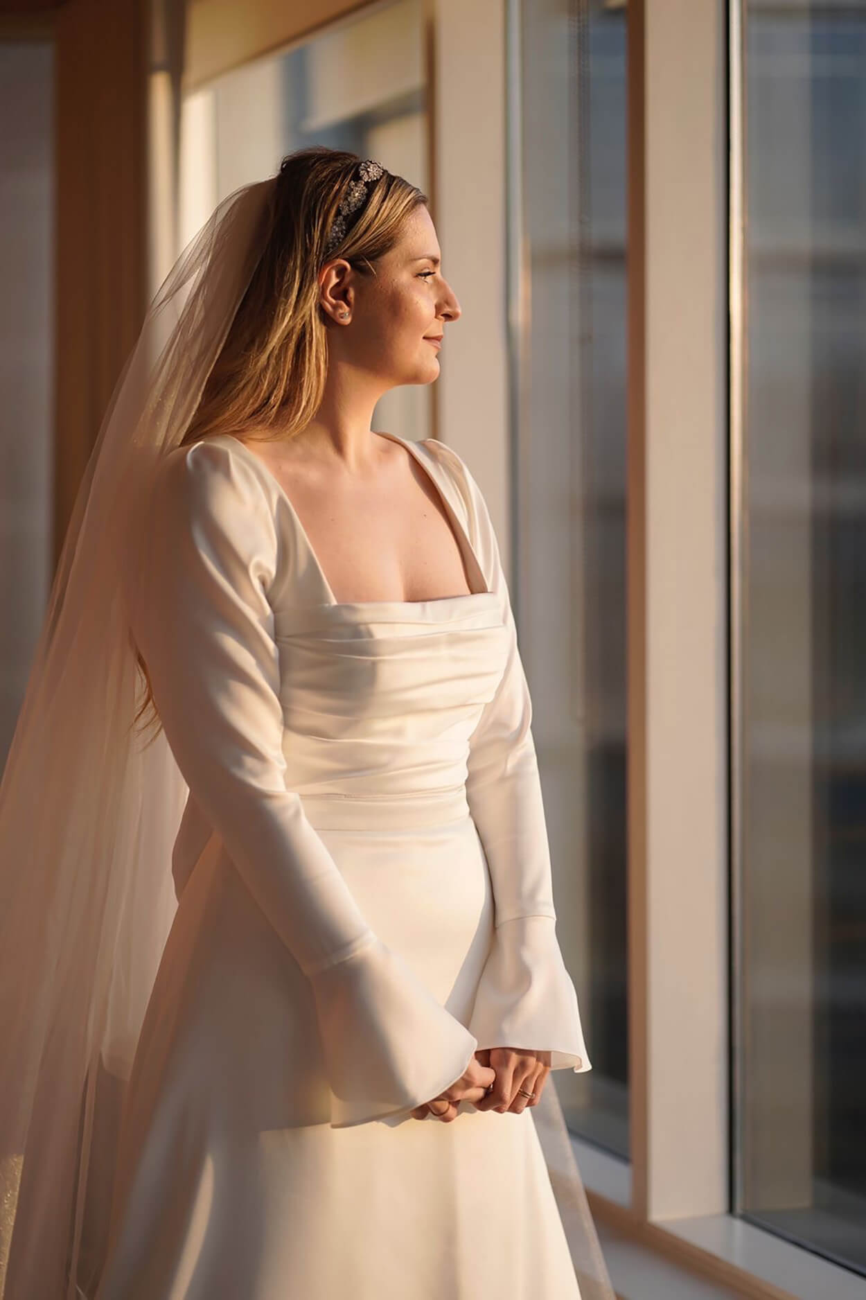 Mulher com vetsido de noiva com manga longa e véu olhando para a janela