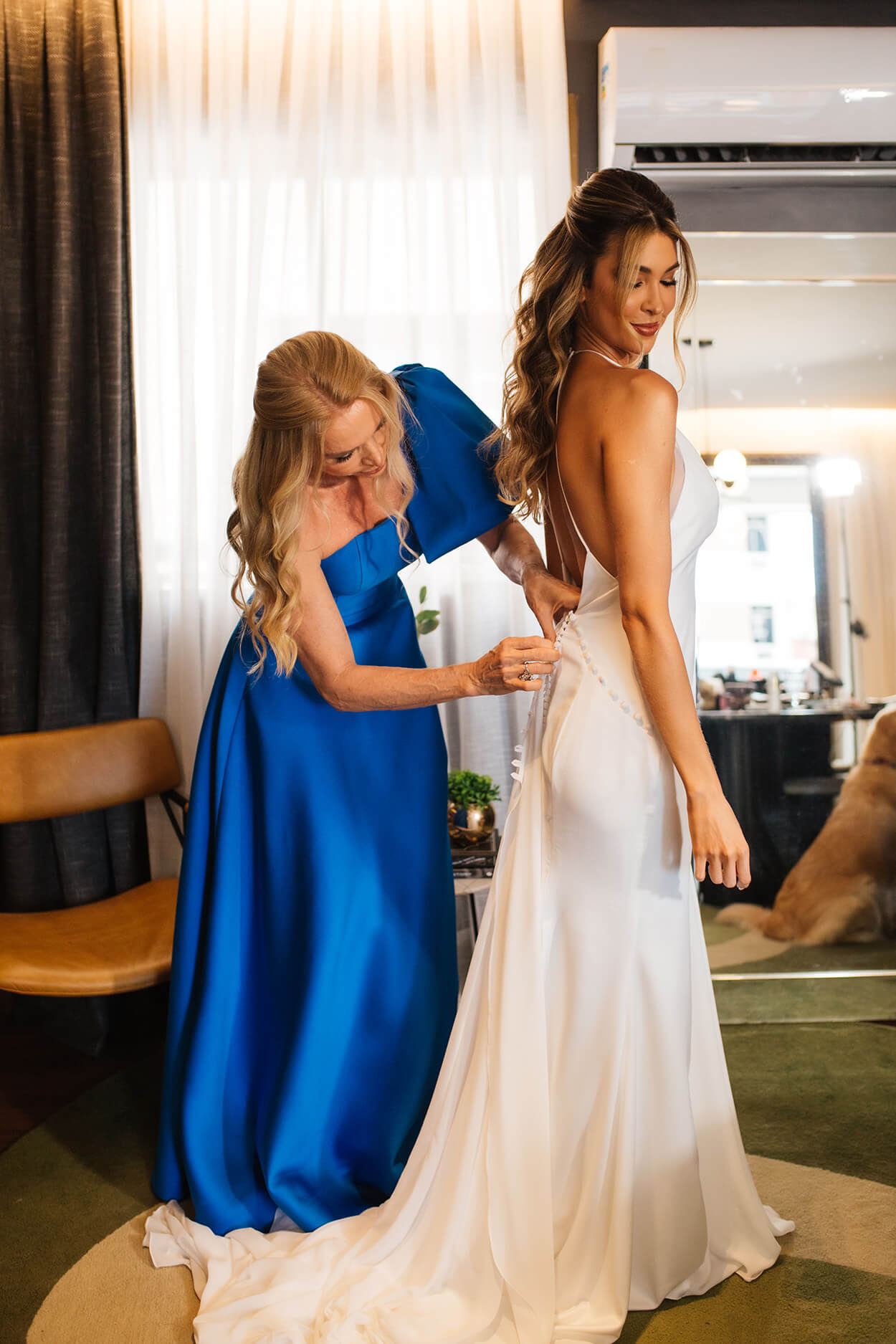 Mãe da noiva com vestido azul ajudando a fechar o vestido dela