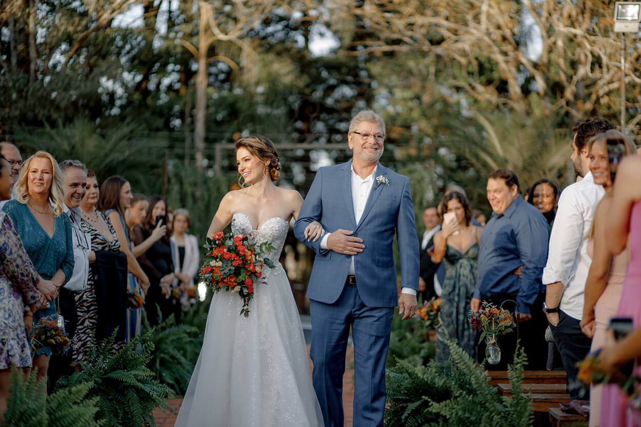 entrada da noiva ao lado do pai com terno azul e flor de lapela branca