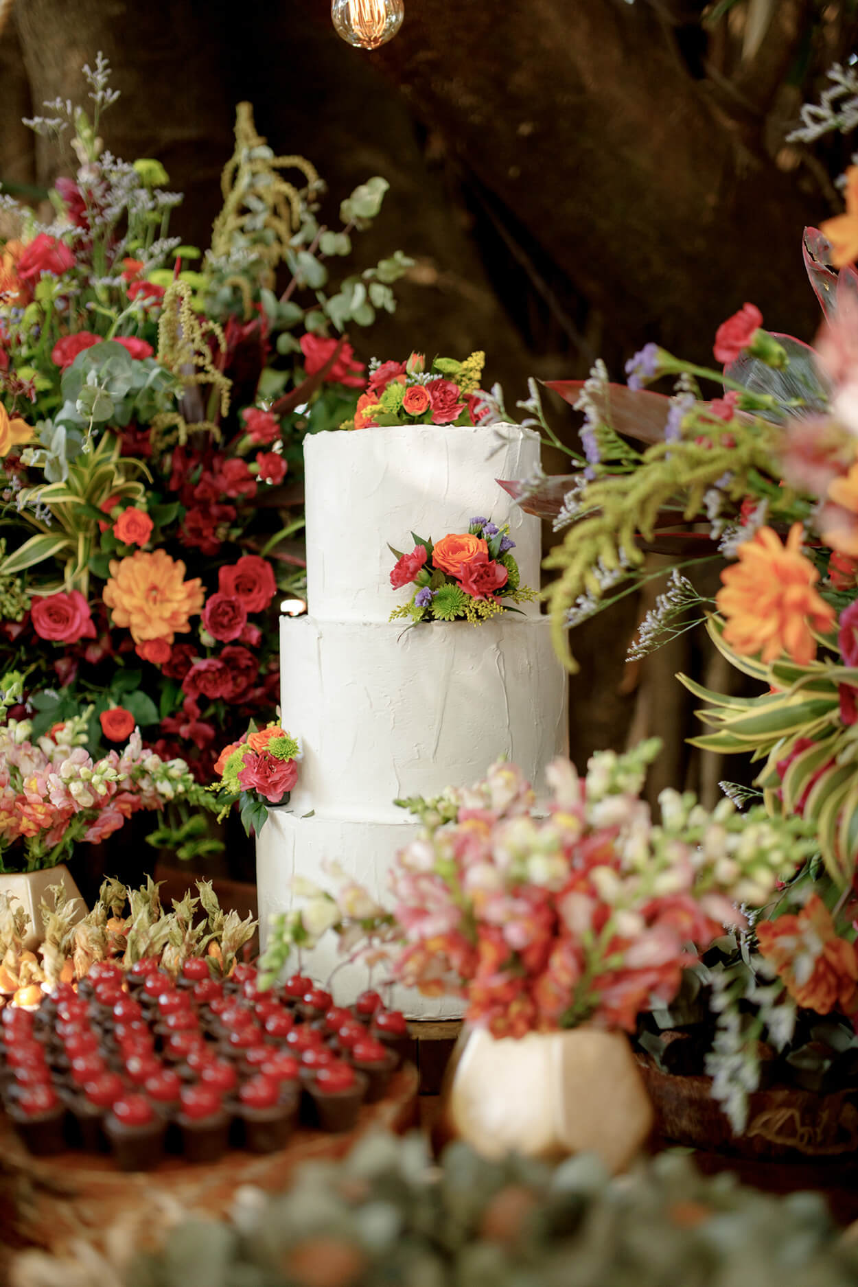 bolo de casamento branco com com três andares e flores vermelhas e laranjas no topo