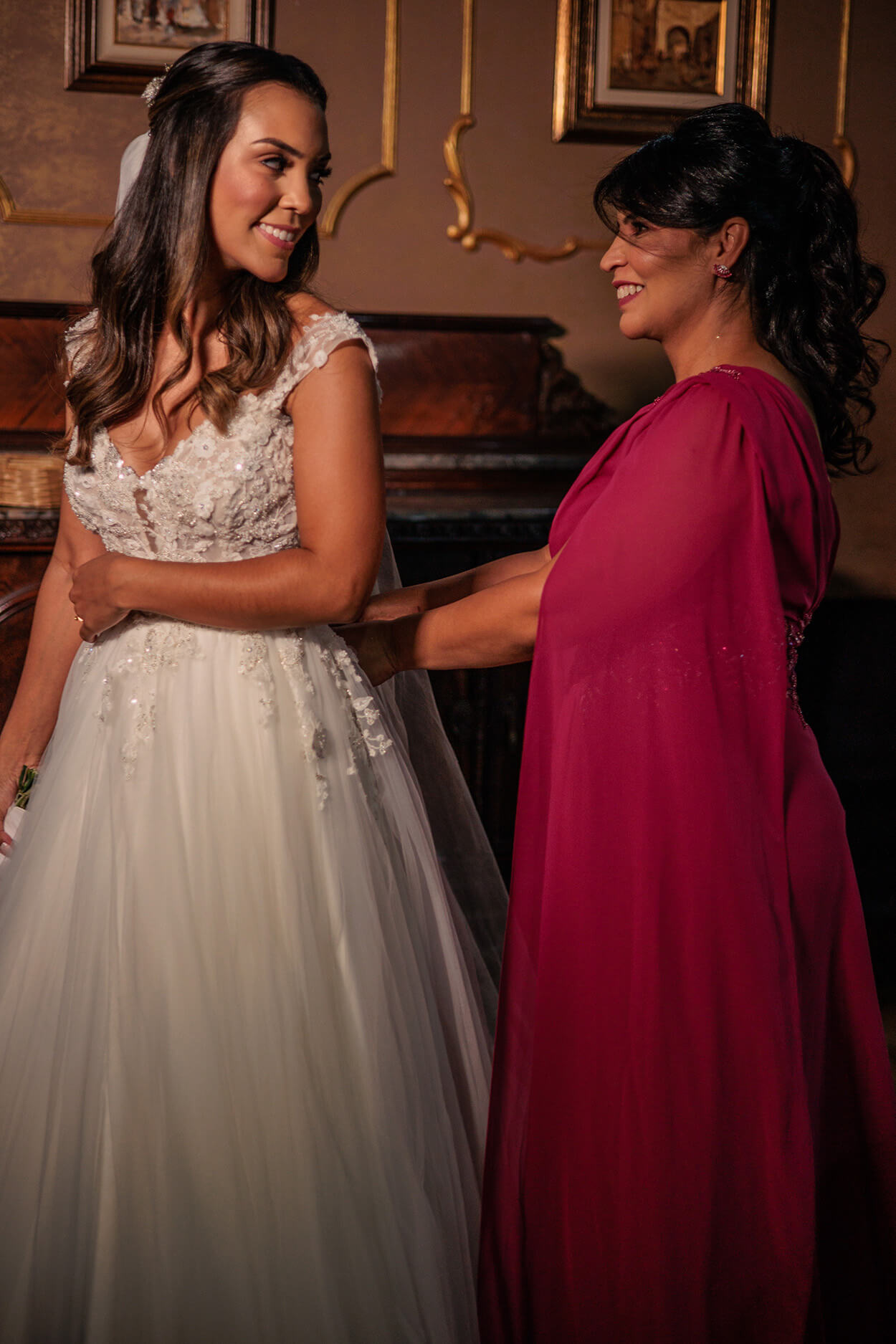 mãe da noiva com vetsido rosa escuro fechando o vestido da noiva