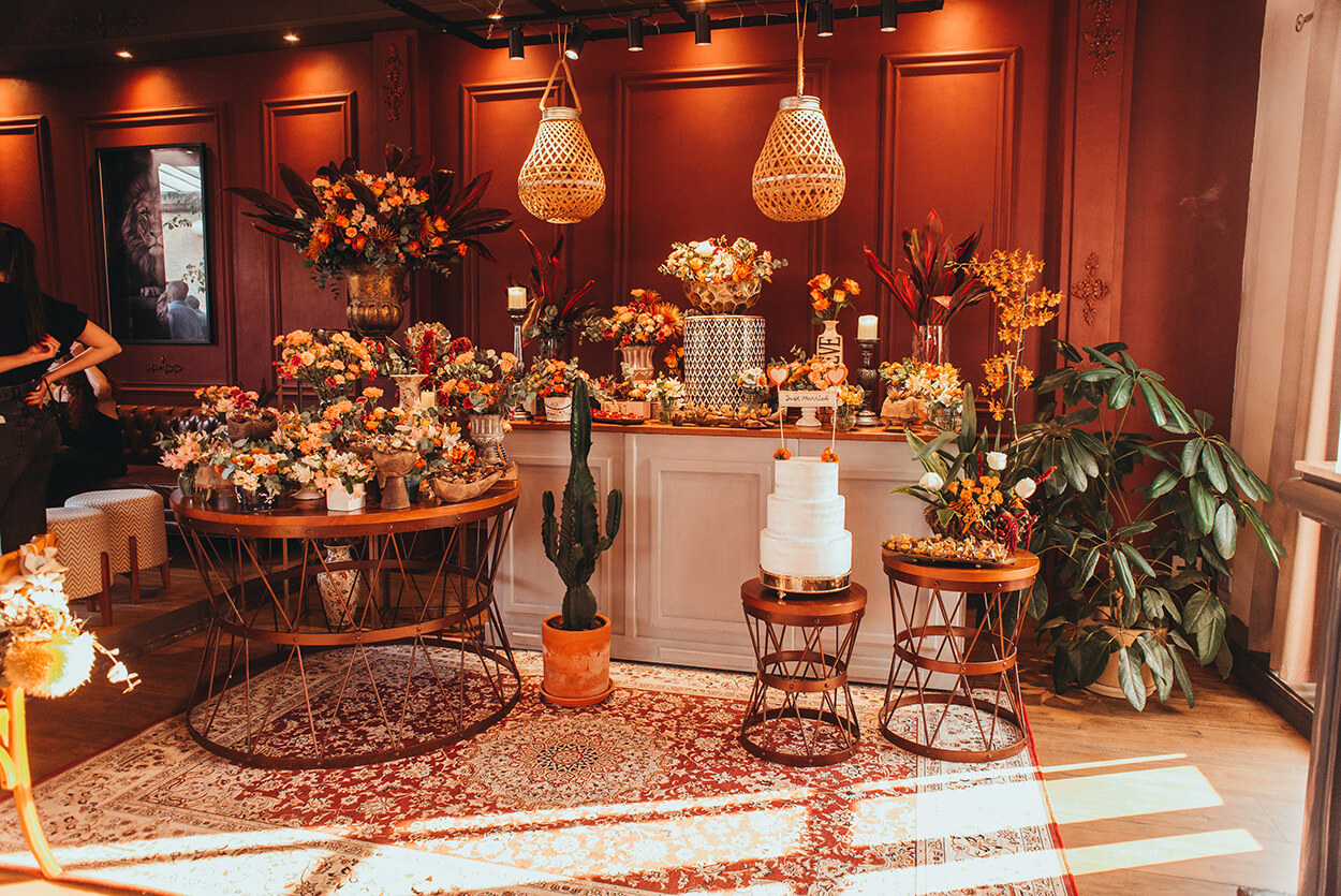 Salão com mesa do bolo e flores laranjas e vermelhas