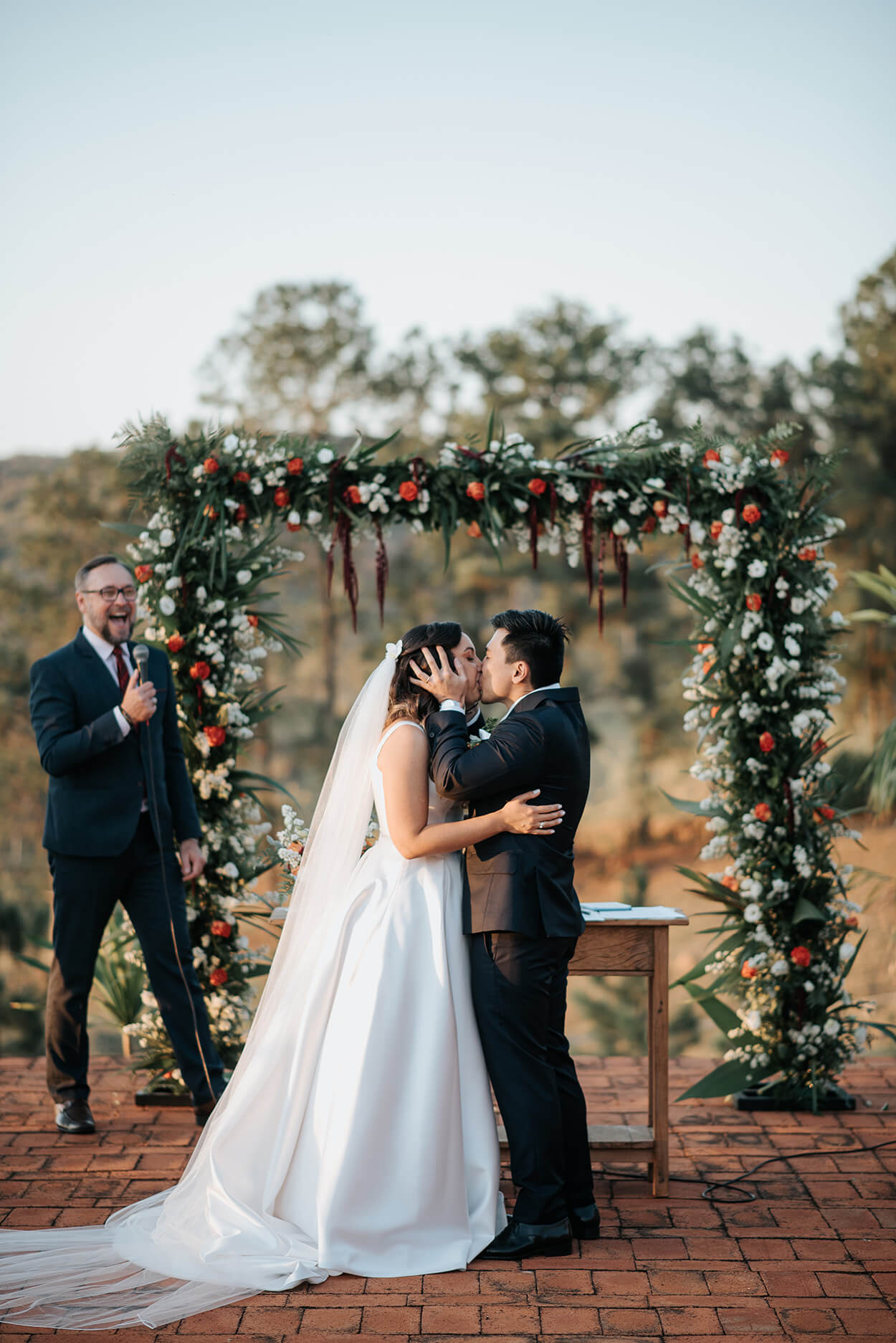 Noivos se beijando no altar com flores brancas e laranjas