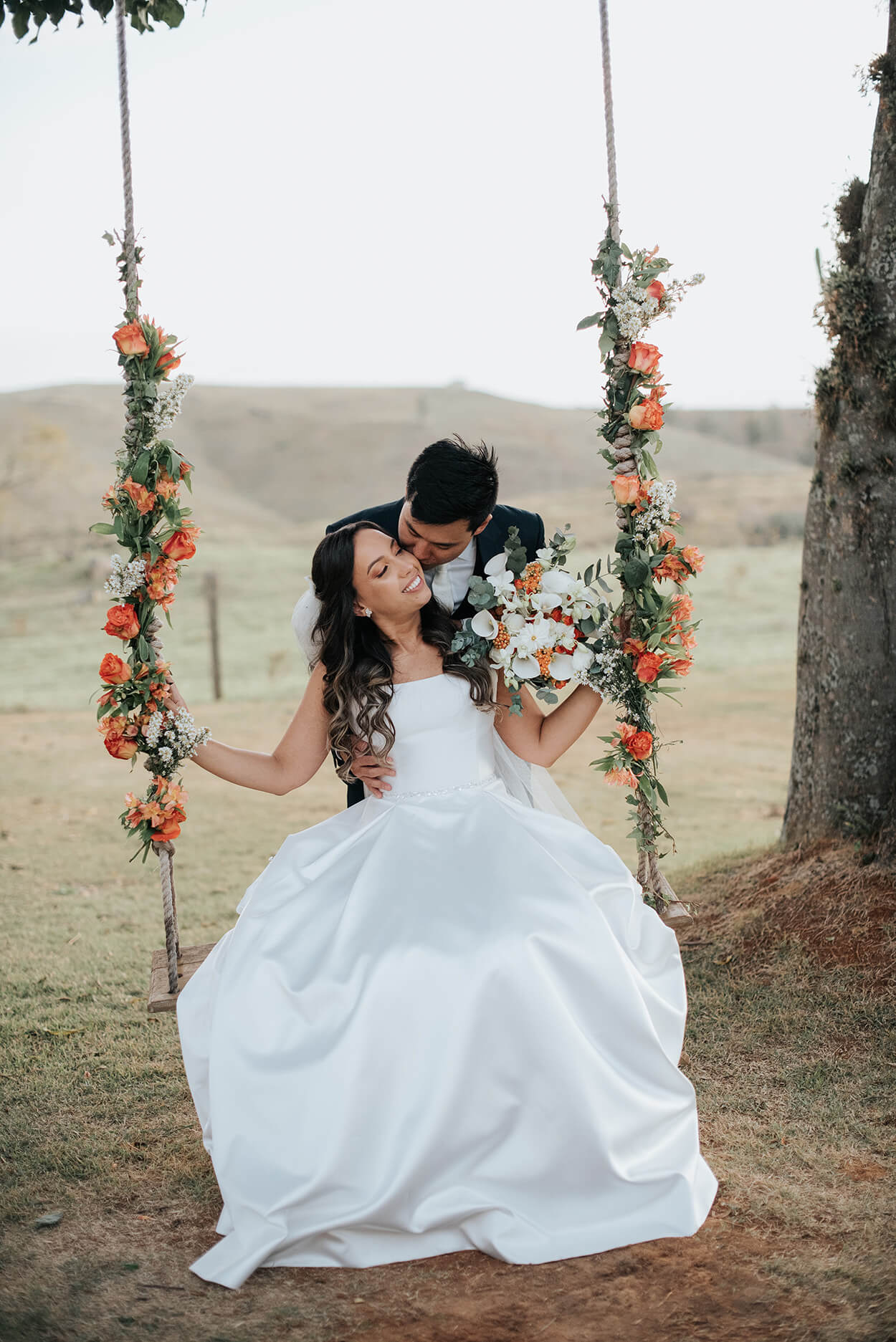 Noivo beijando a noiva sentada no balanço com flores