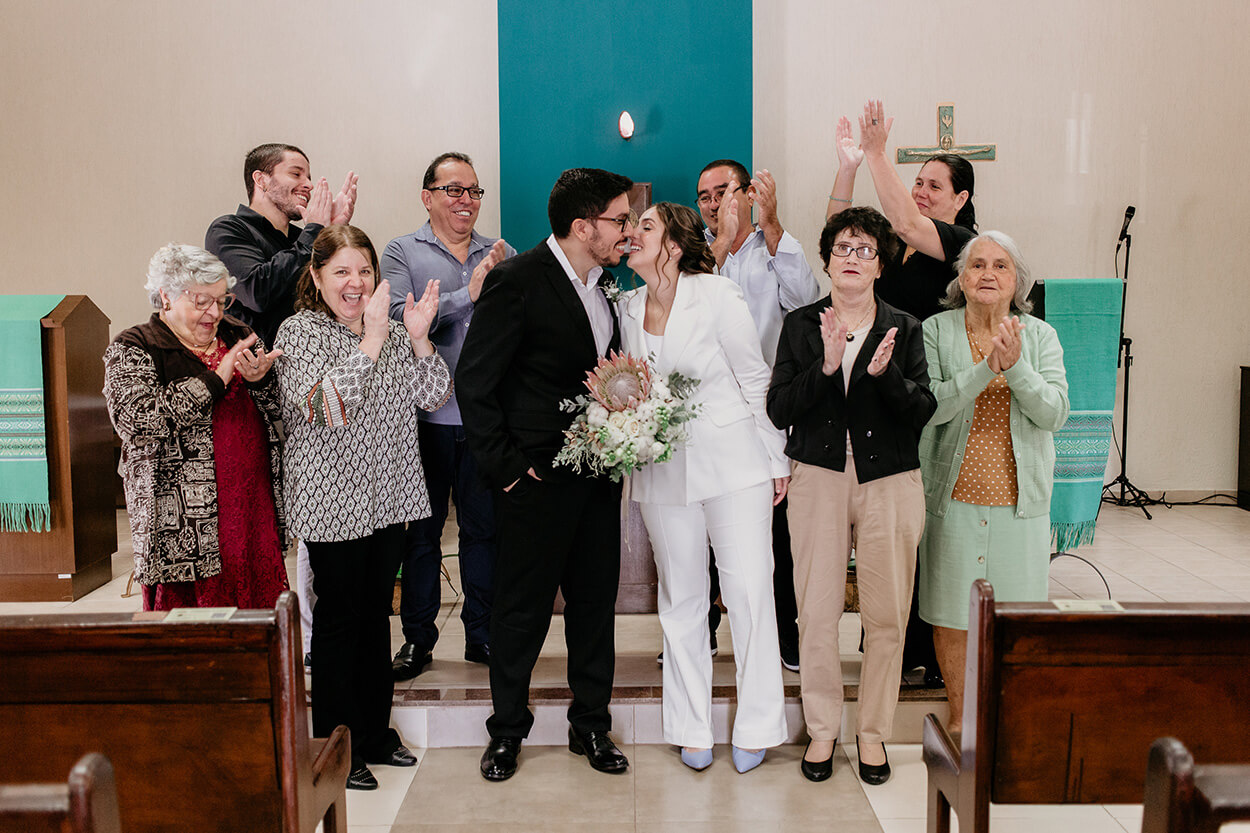noivos se beijando e convidados batendo palmas na igreja