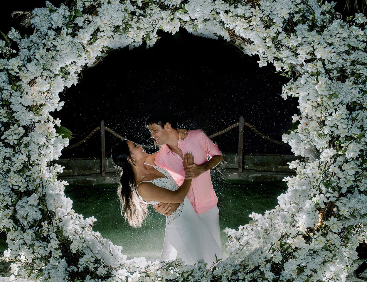 noivos abraçados atrás do arco com flores brancas