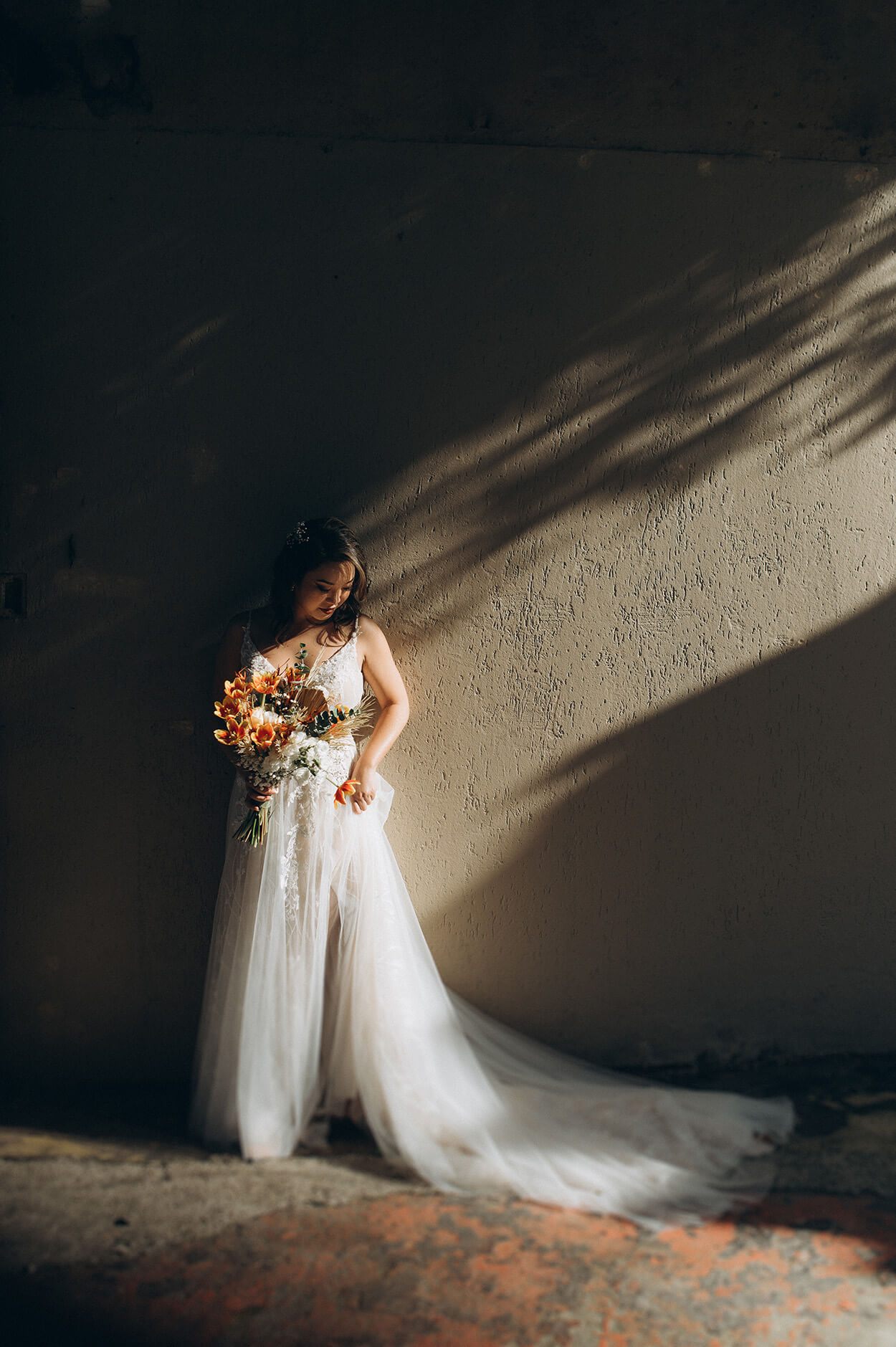 Noiva com cauda longa segurando buquê com flores brancas e laranjas