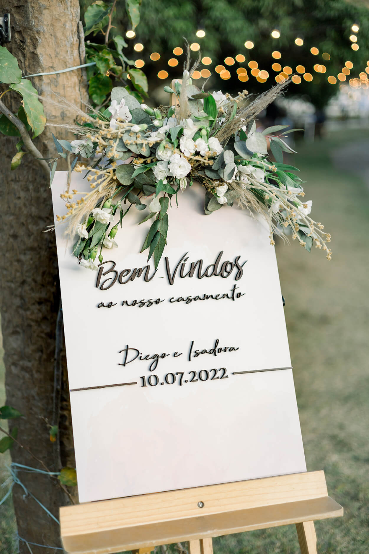 cavalete com placa escrito bem-vindos com arranjo de flores brancas