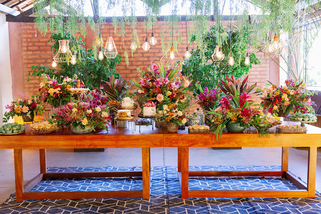 Mesa de madeira com flores rosas e amarelas e trio de bolos de casamento