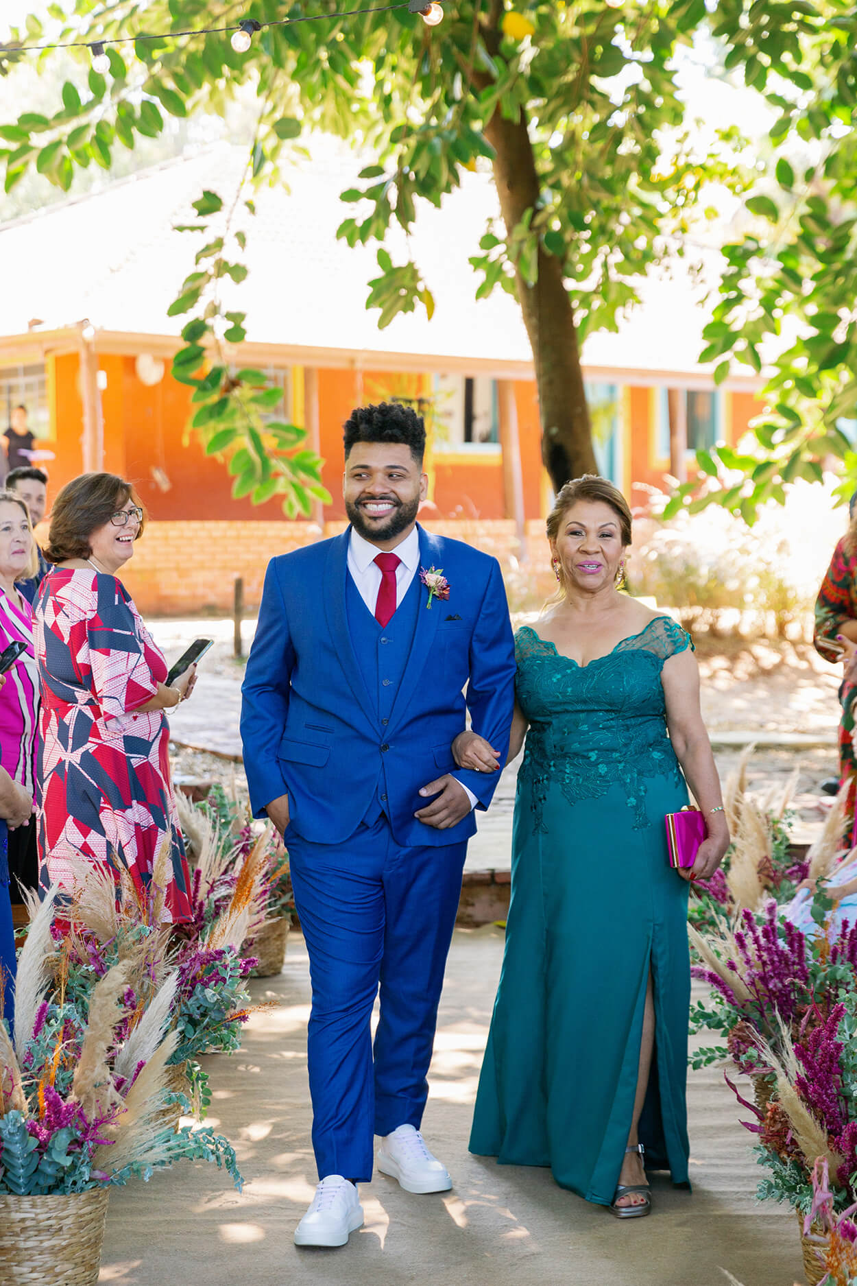 entrada do noivo com terno azul ao lado da mãe com vestido verde