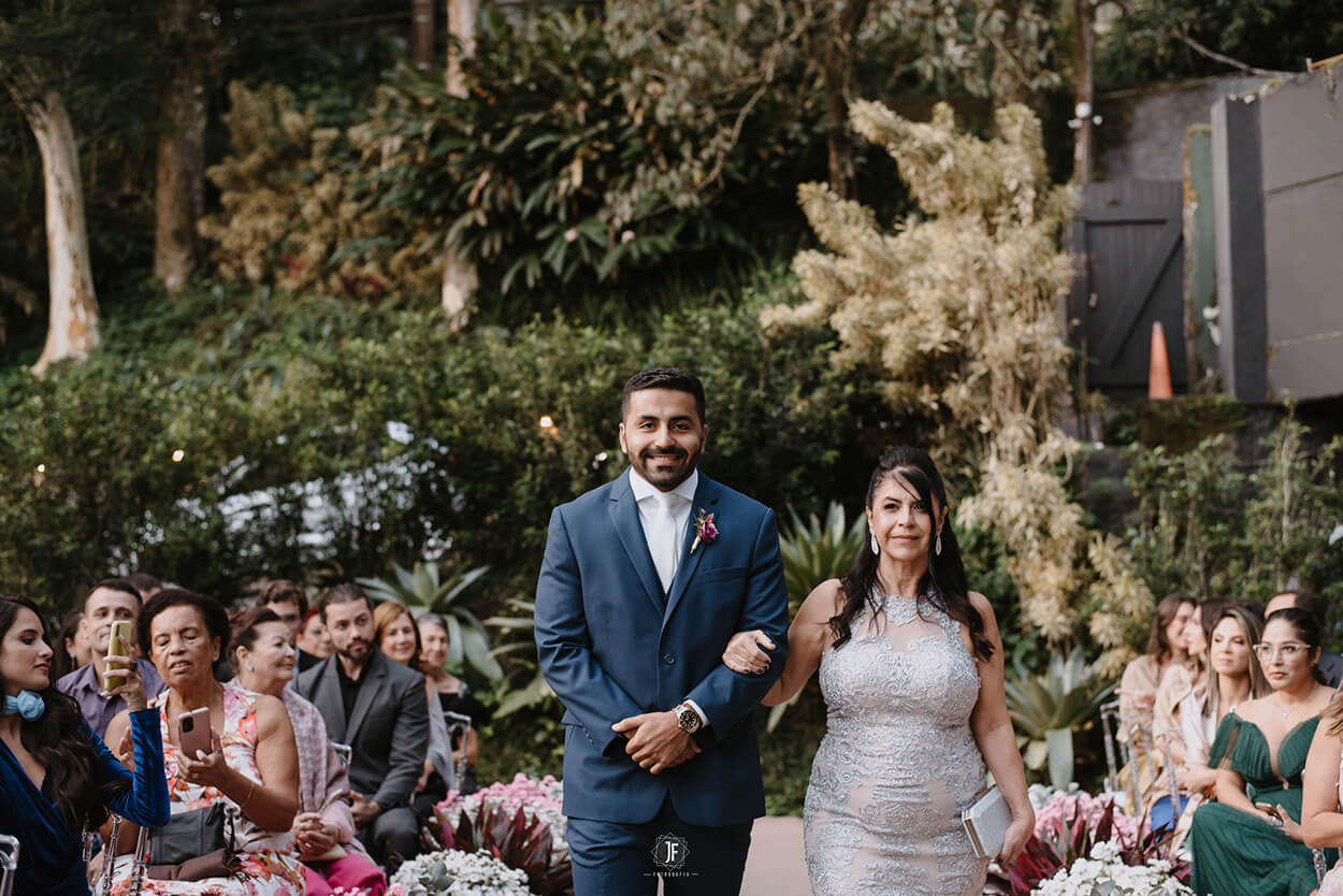 entrada do noivo com o terno azul ao lado da mãe com vetsido branco