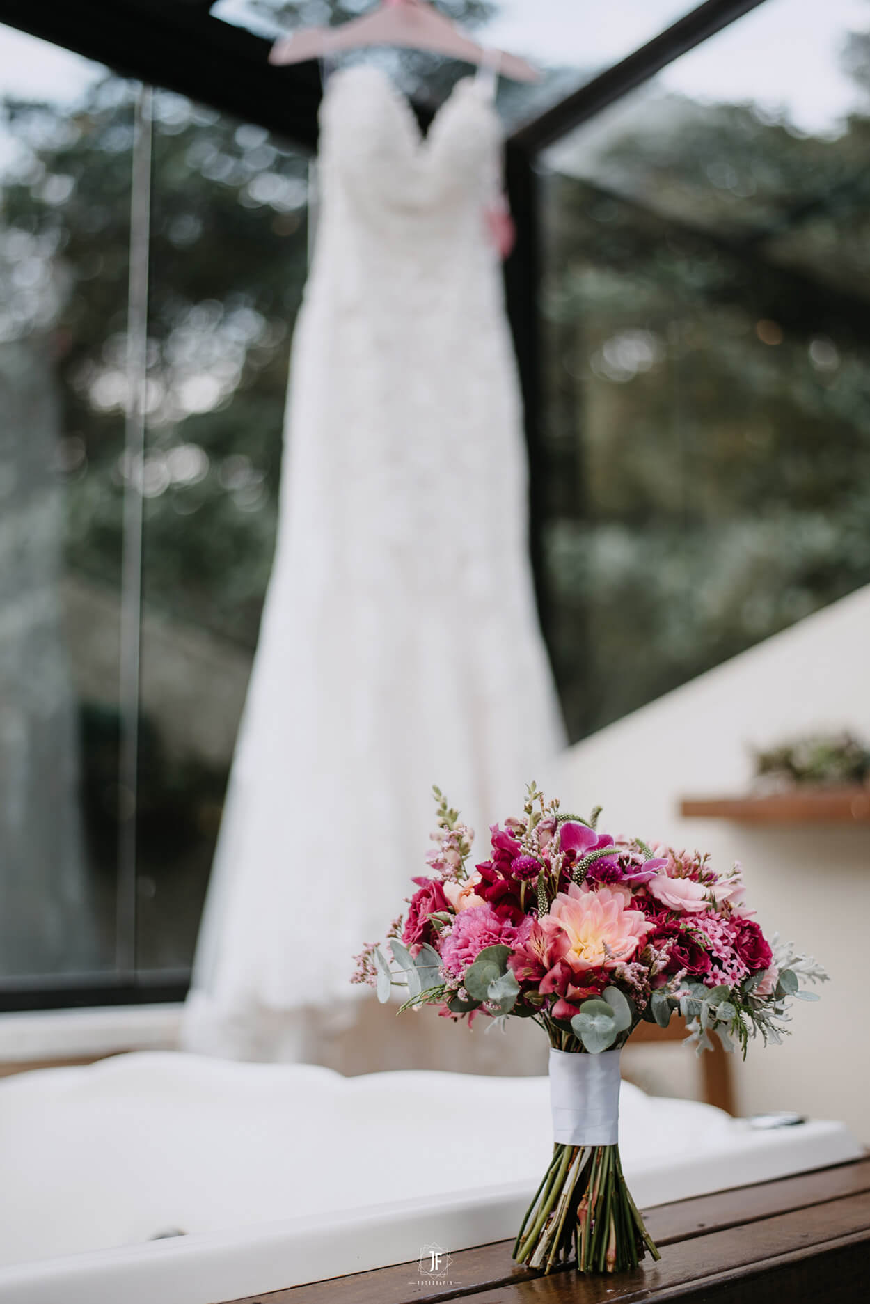 vestido de noiva pendurado no cabide e buquê cor de rosa e roxo