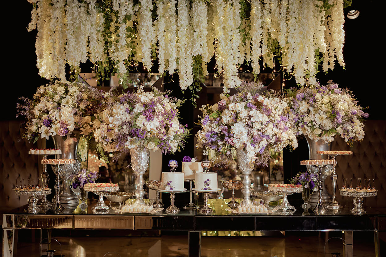 mesa com trio de bolos de casamento e vasos com flroes brancas e roxas