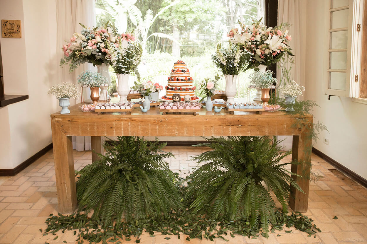 mesa de madeira com bolo naked cake com vasos de flores brancas e cor de rosa