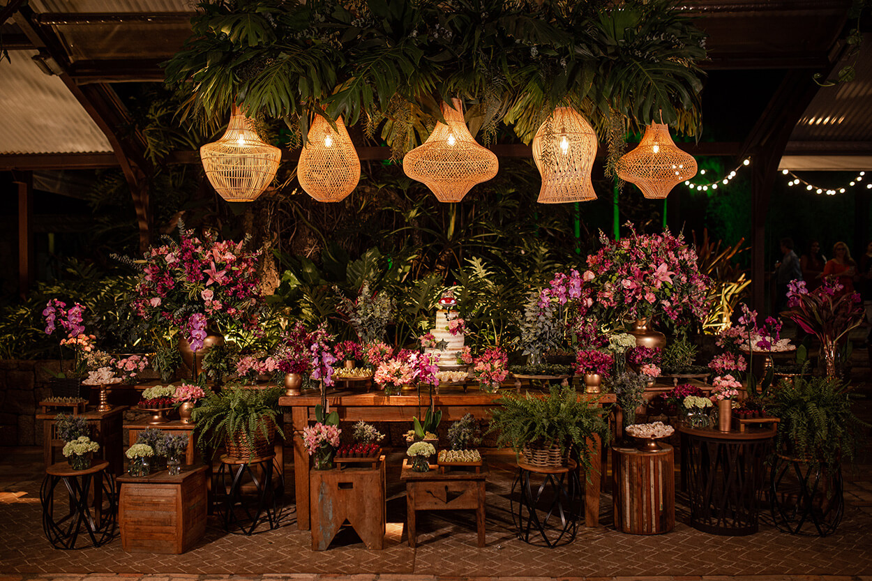 Mesas de madeira com vasos com flores rosas e bolo de casamento com tres andares