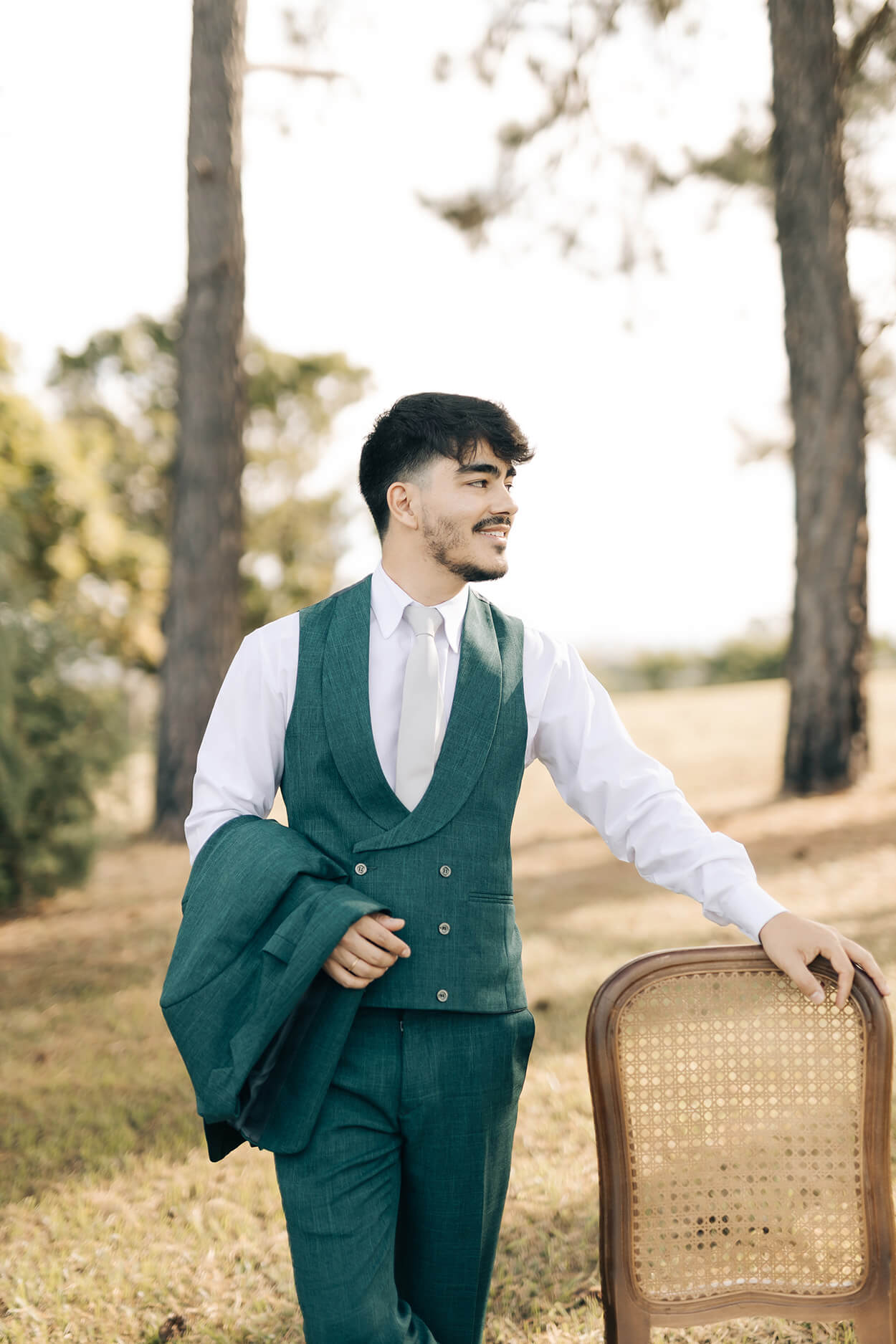 noivo com colete verde e gravata cinza apoiado na cadeira no campo